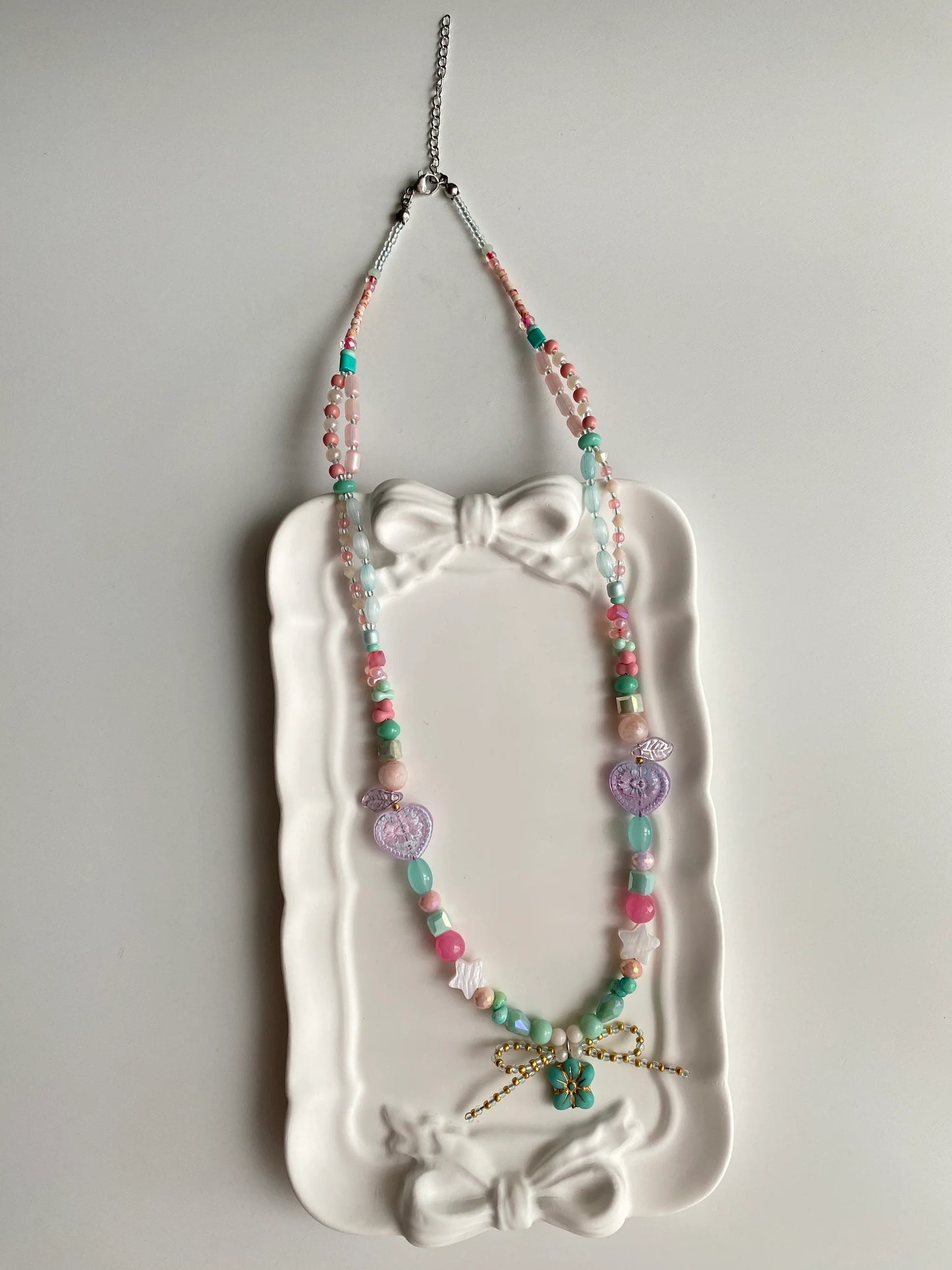 HuibenCraft 1-of-1 bright and playful layered necklace with pink and blue beads in a white ceramic dish under natural sunlight.