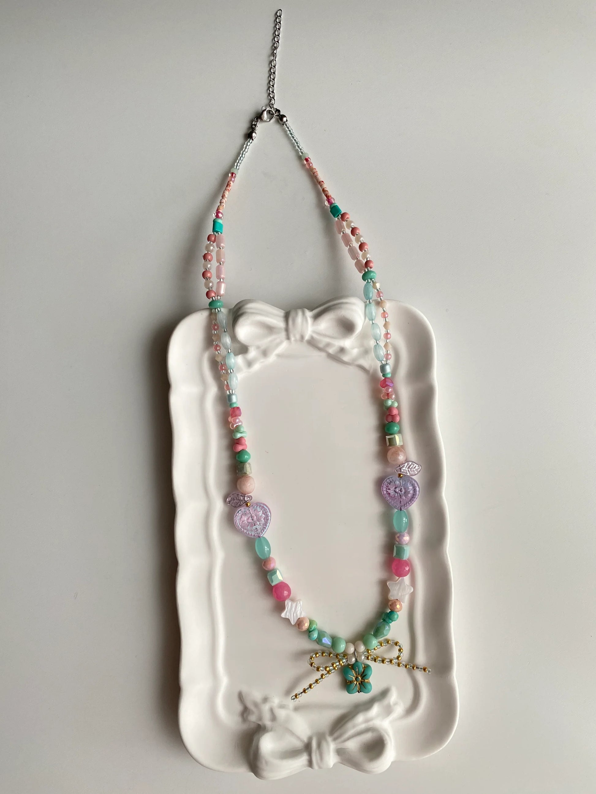 HuibenCraft 1-of-1 bright and playful layered necklace with pink and blue beads in a white ceramic dish under natural sunlight.