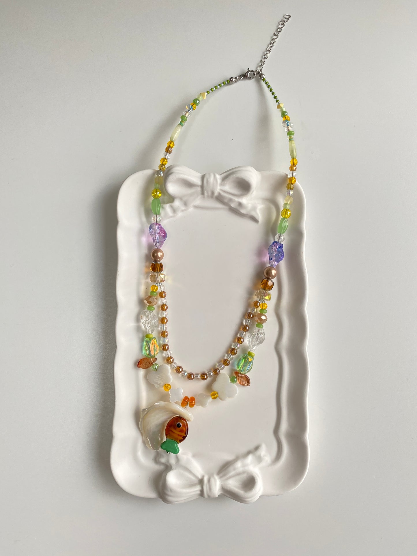 Brown and green Czech glass fish necklace displayed flat, featuring a natural Triton shell pendant, layered beadwork and ocean bubble-inspired details.