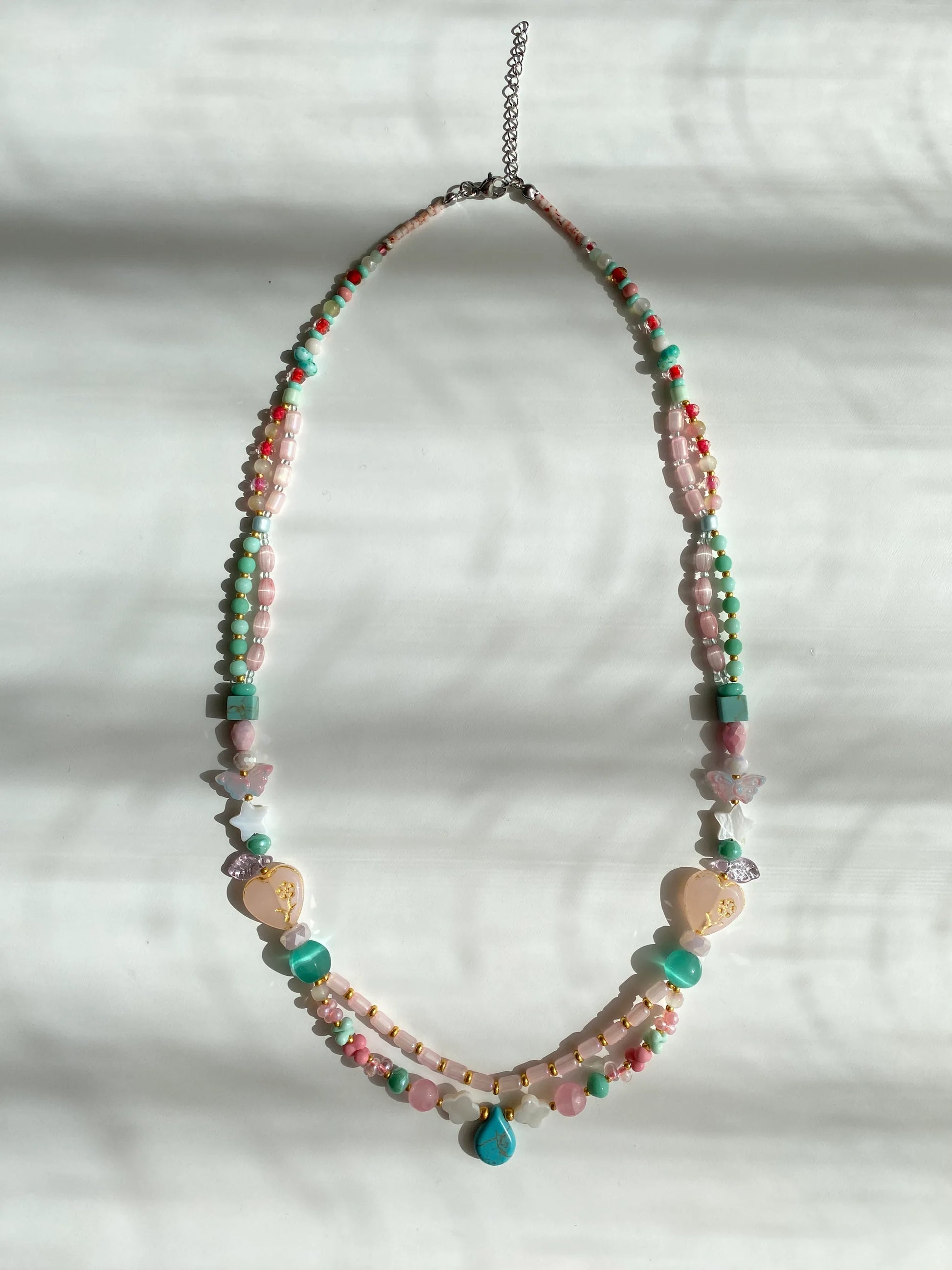 Detailed view of a handcrafted vibrant necklace featuring a crimson ceramic vase overflowing with 3D beaded flowers on a sunlit white desk.