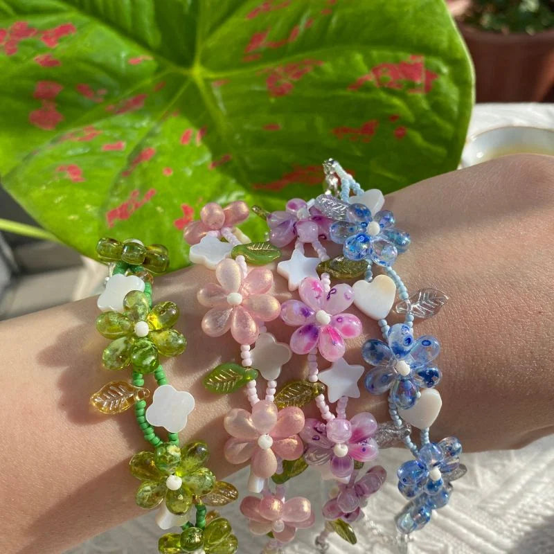 A vibrant collection of HuibenCraft handmade bead-woven flower bracelets in blue, green, and pink, featuring shell charms in clover, star, and heart shapes for a whimsical look.