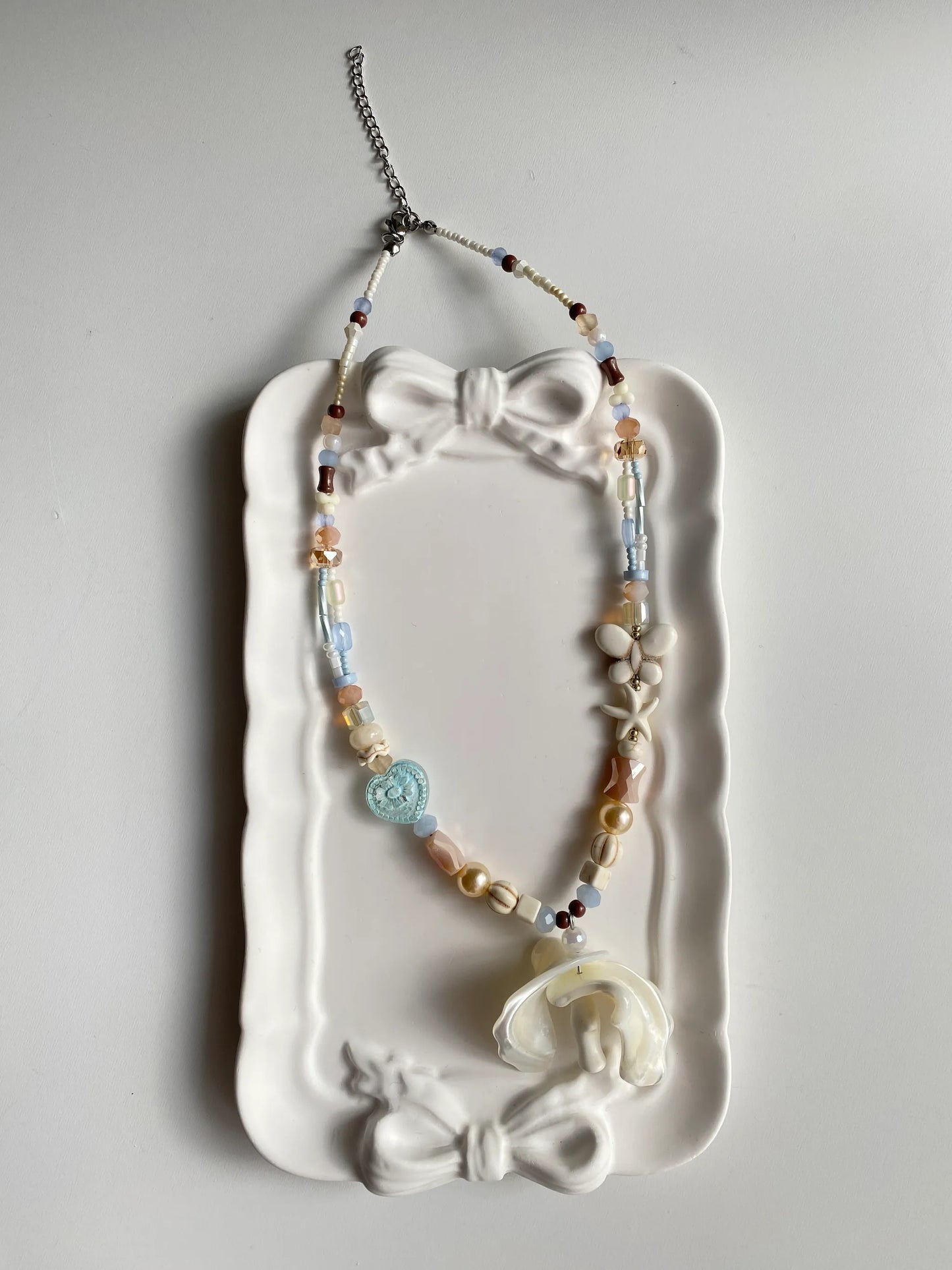 HuibenCraft 1-of-1 vibrant coastal-inspired beaded necklace with a statement shell pendant in a white ceramic dish, reflecting a sunny holiday vibe.