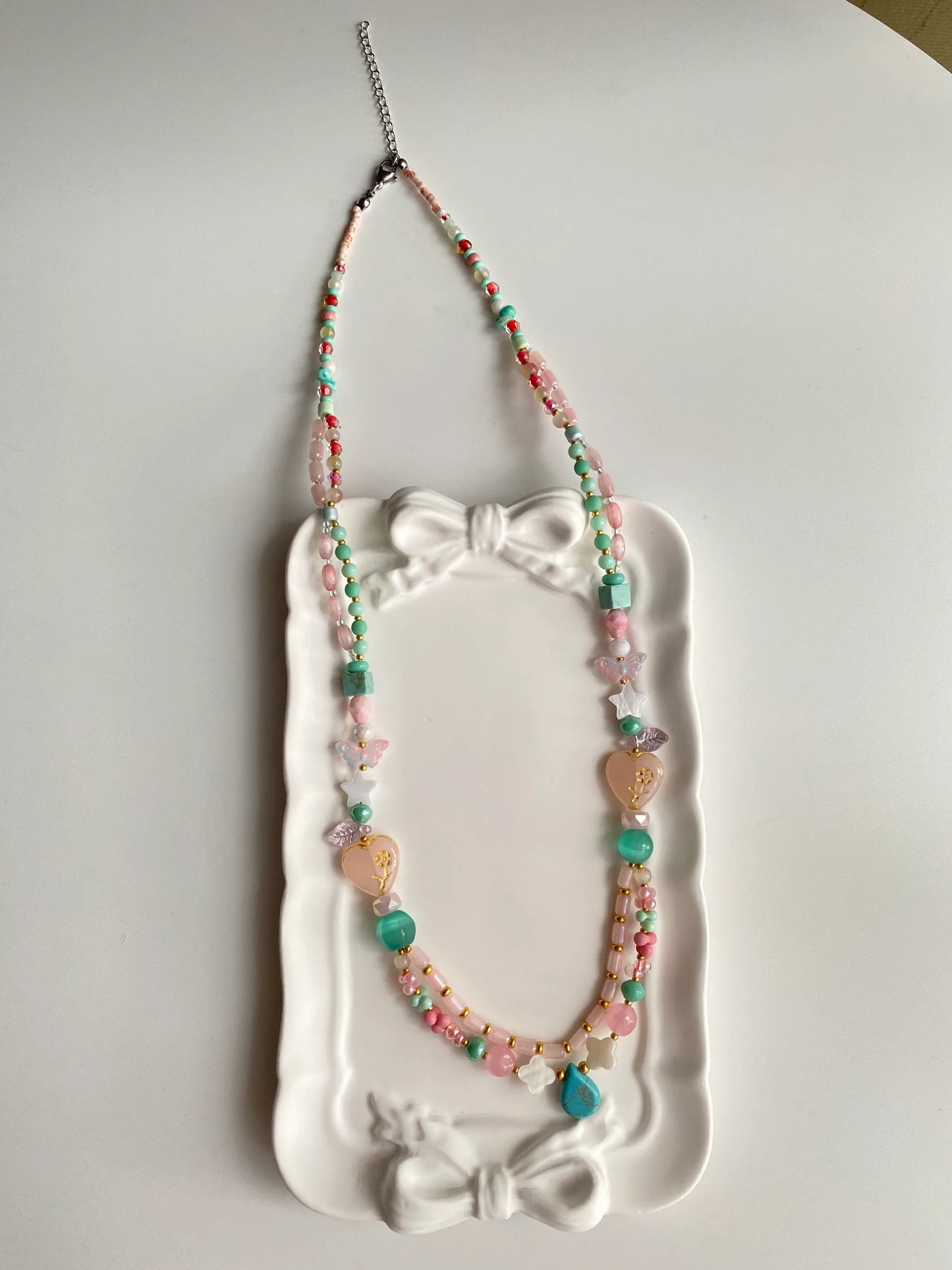 HuibenCraft 1-of-1 vibrant bohemian-style long necklace with diverse glass charms in a white ceramic dish, a unique artisanal gift.
