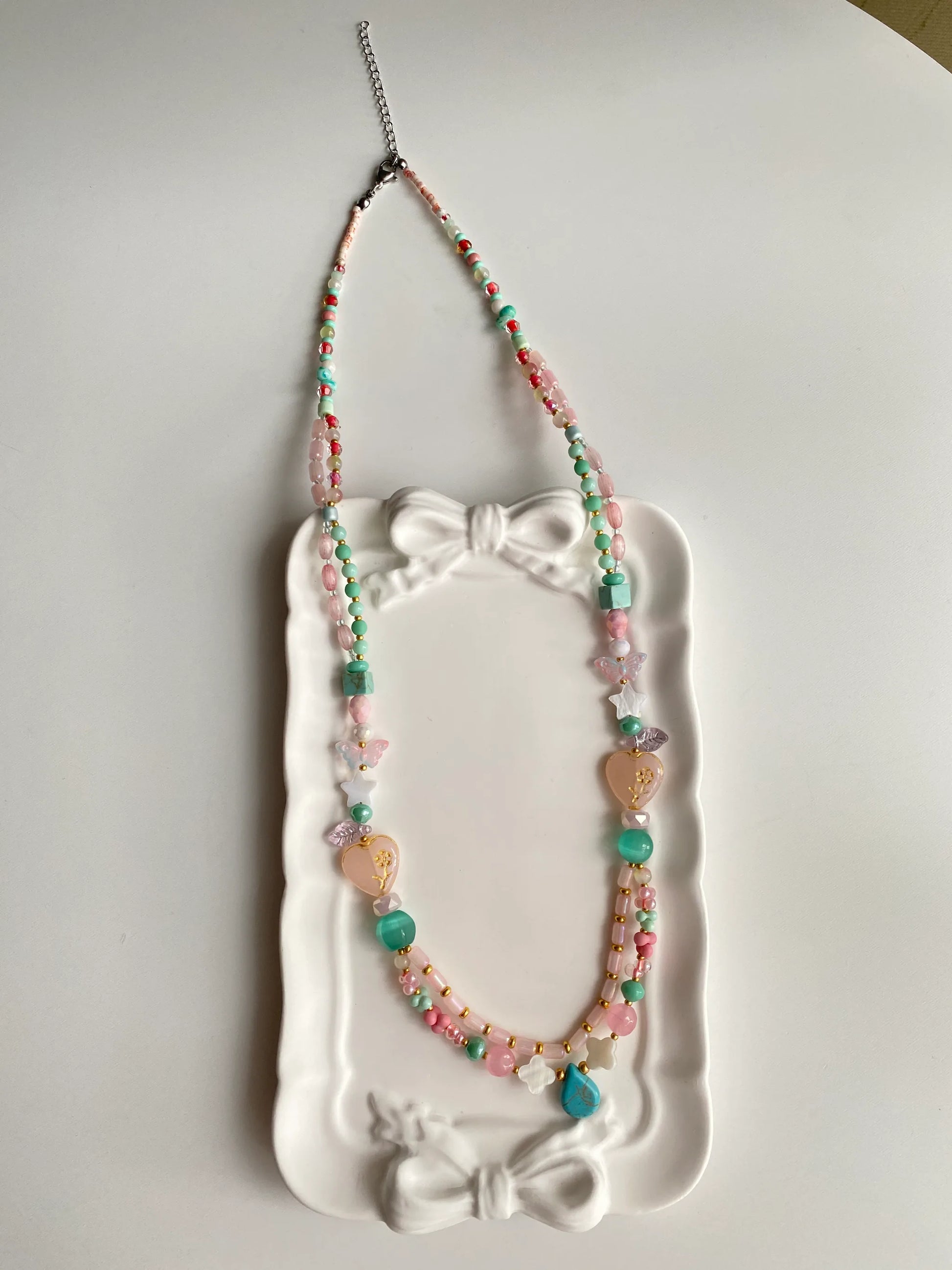 HuibenCraft 1-of-1 vibrant bohemian-style long necklace with diverse glass charms in a white ceramic dish, a unique artisanal gift.