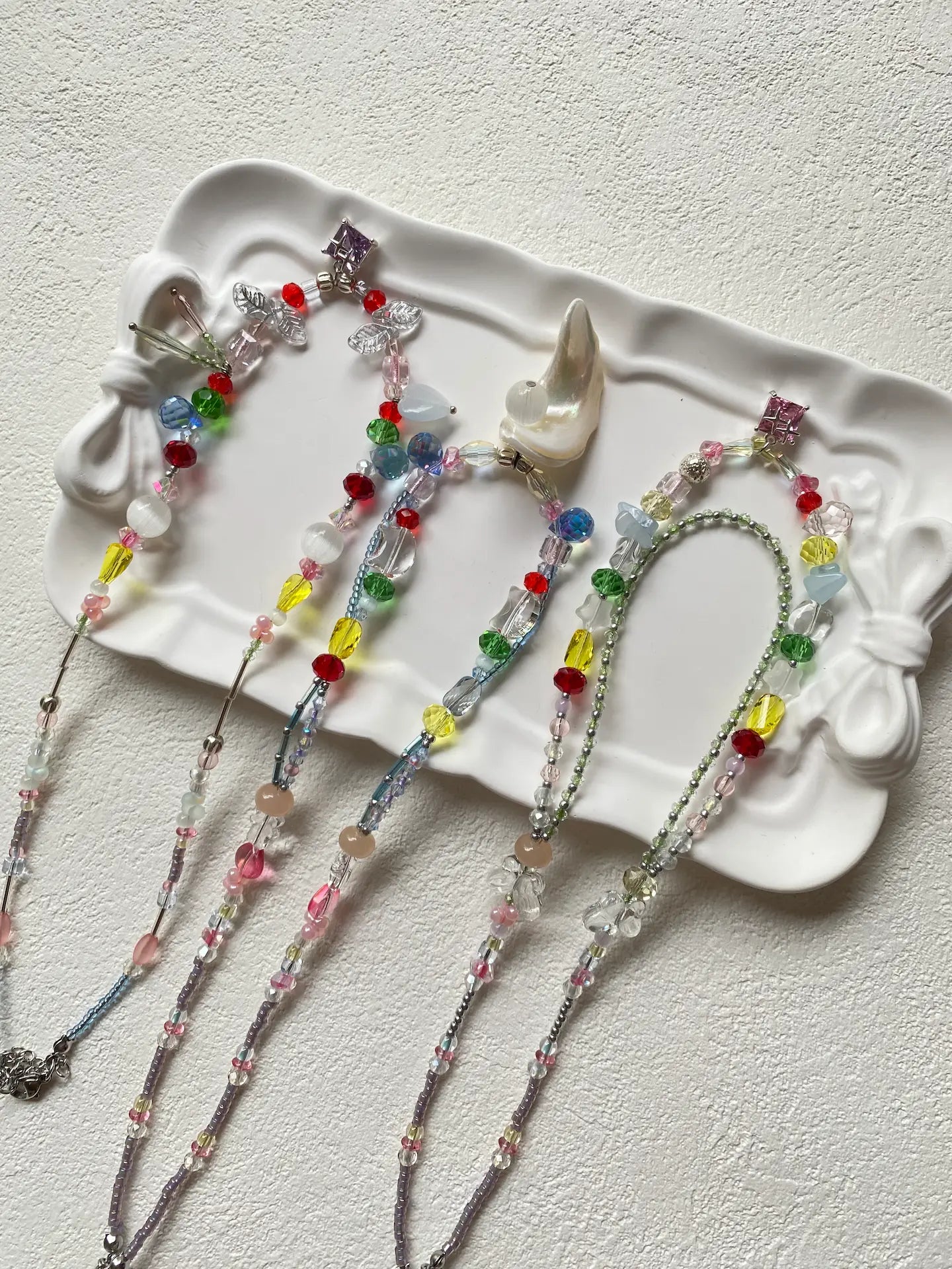 HuibenCraft trio of colorful artisan seed bead necklaces arranged as a flat lay in a ceramic plate, top-down view showing unique 1-of-1 designs.