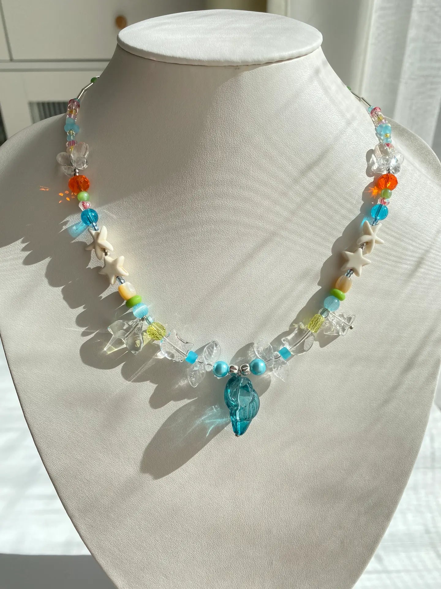 A playful ocean necklace with a blue conch and kitty head charms, showcased on a jewelry mannequin neck.
