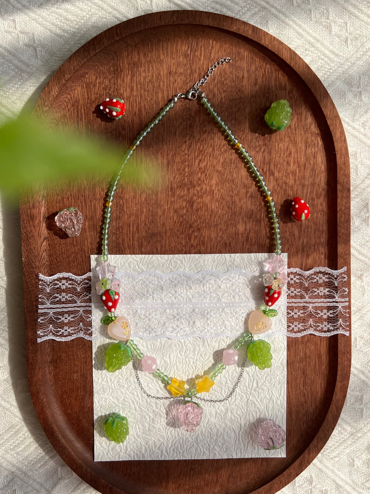 Cute Raspberry Strawberry Necklace arranged on a wooden tray with raspberry beads nearby.