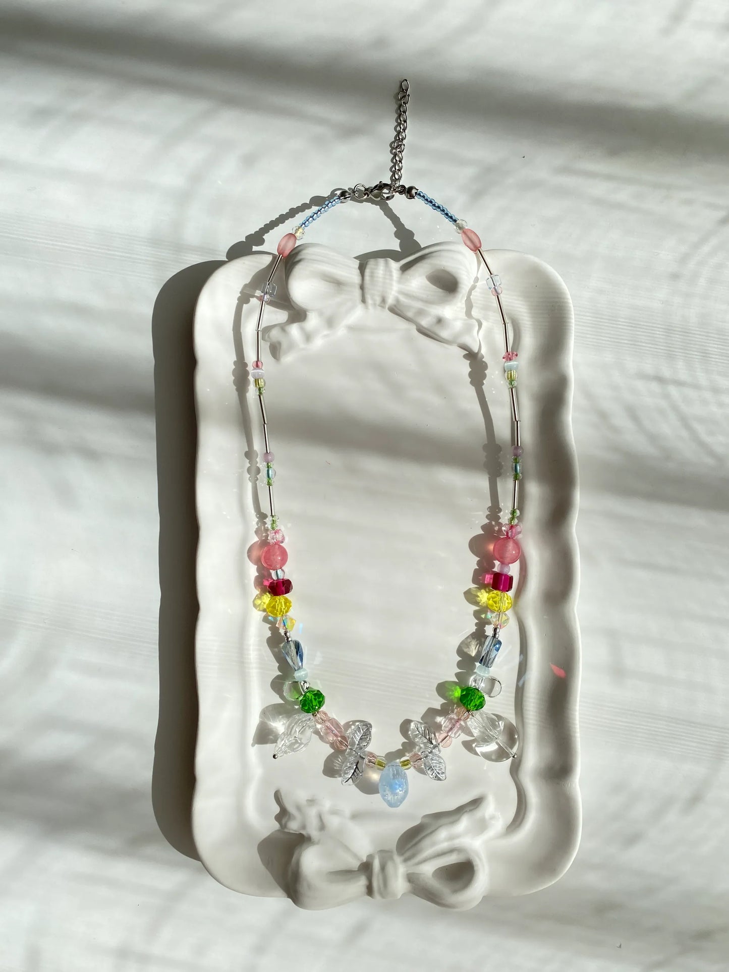 Unique HuibenCraft artisan necklace with a transparent blue-white lemon pendant and silver leaf beads, beautifully displayed in a small dish under natural light.