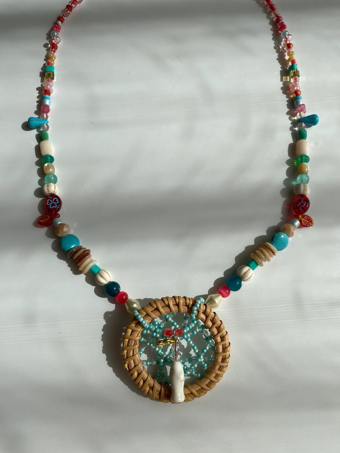 Close-up of a heavy-workmanship dreamcatcher pendant with a delicate beaded web and a white pine stone fish at the center.