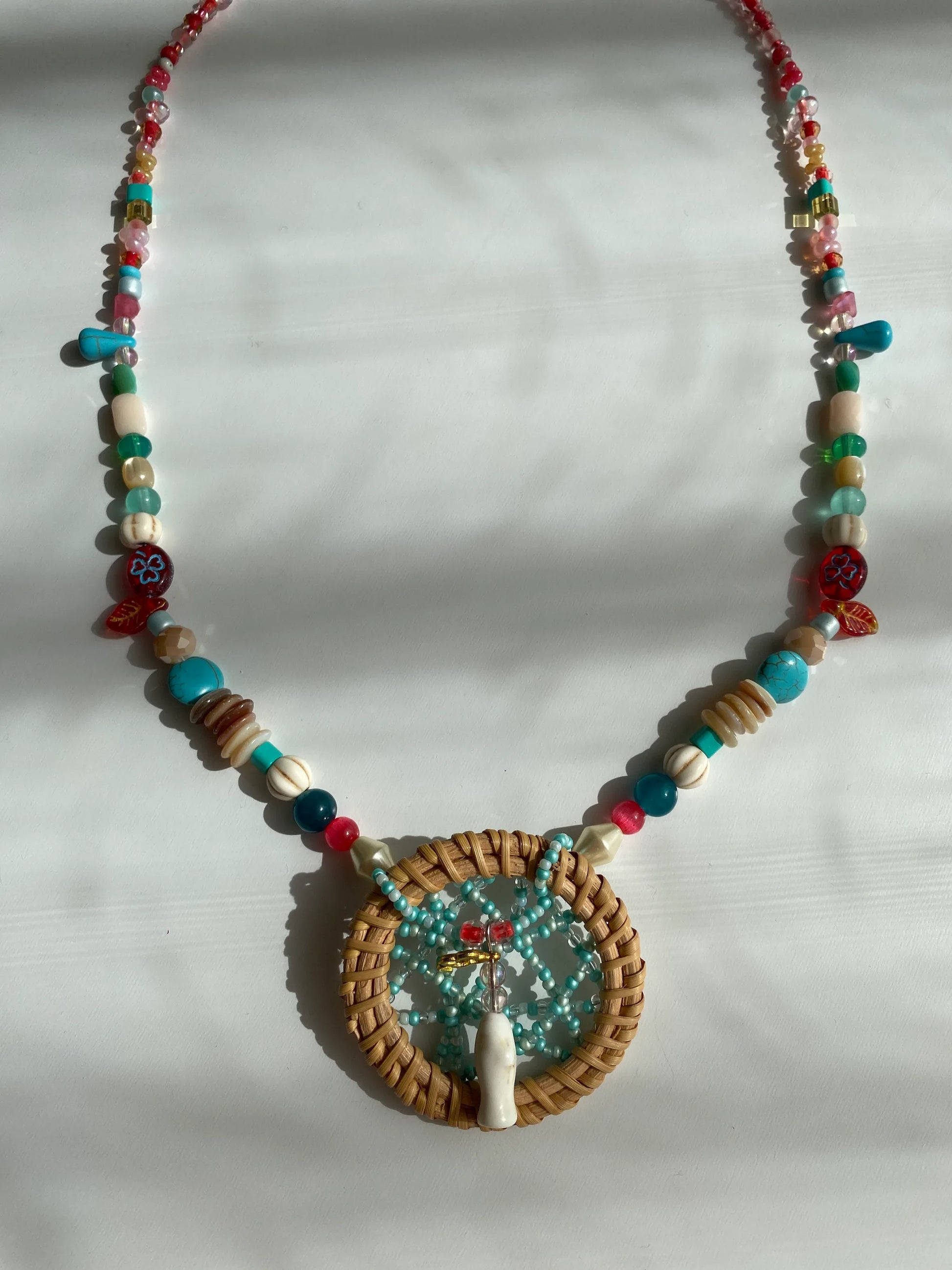 Close-up of a heavy-workmanship dreamcatcher pendant with a delicate beaded web and a white pine stone fish at the center.
