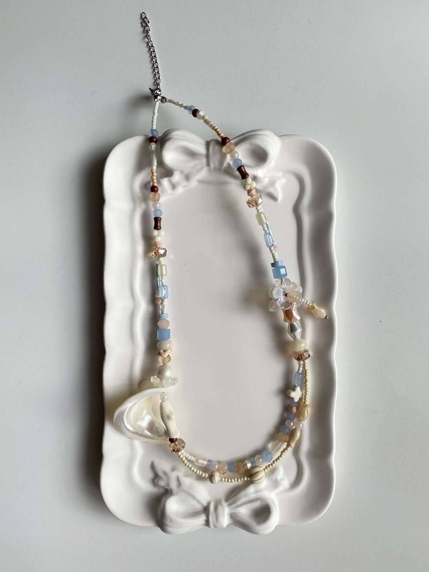 HuibenCraft 1-of-1 dreamy seaside-inspired layered necklace with diverse coastal charms in a white ceramic dish, a unique artisan gift.