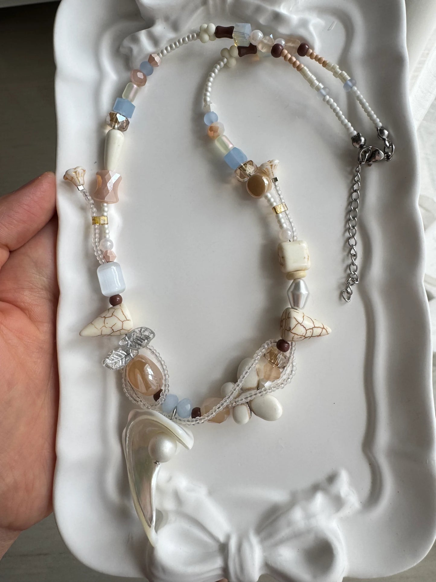 HuibenCraft 1-of-1 ethereal ocean-inspired necklace with a statement shell-and-bead pendant in a white ceramic dish under natural light.