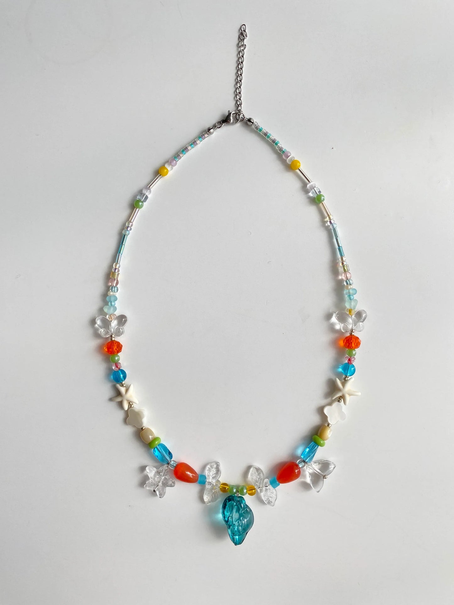 Close-up of white glass fishtail and blue conch charms sparkling under the sun, showcasing artisanal textures.