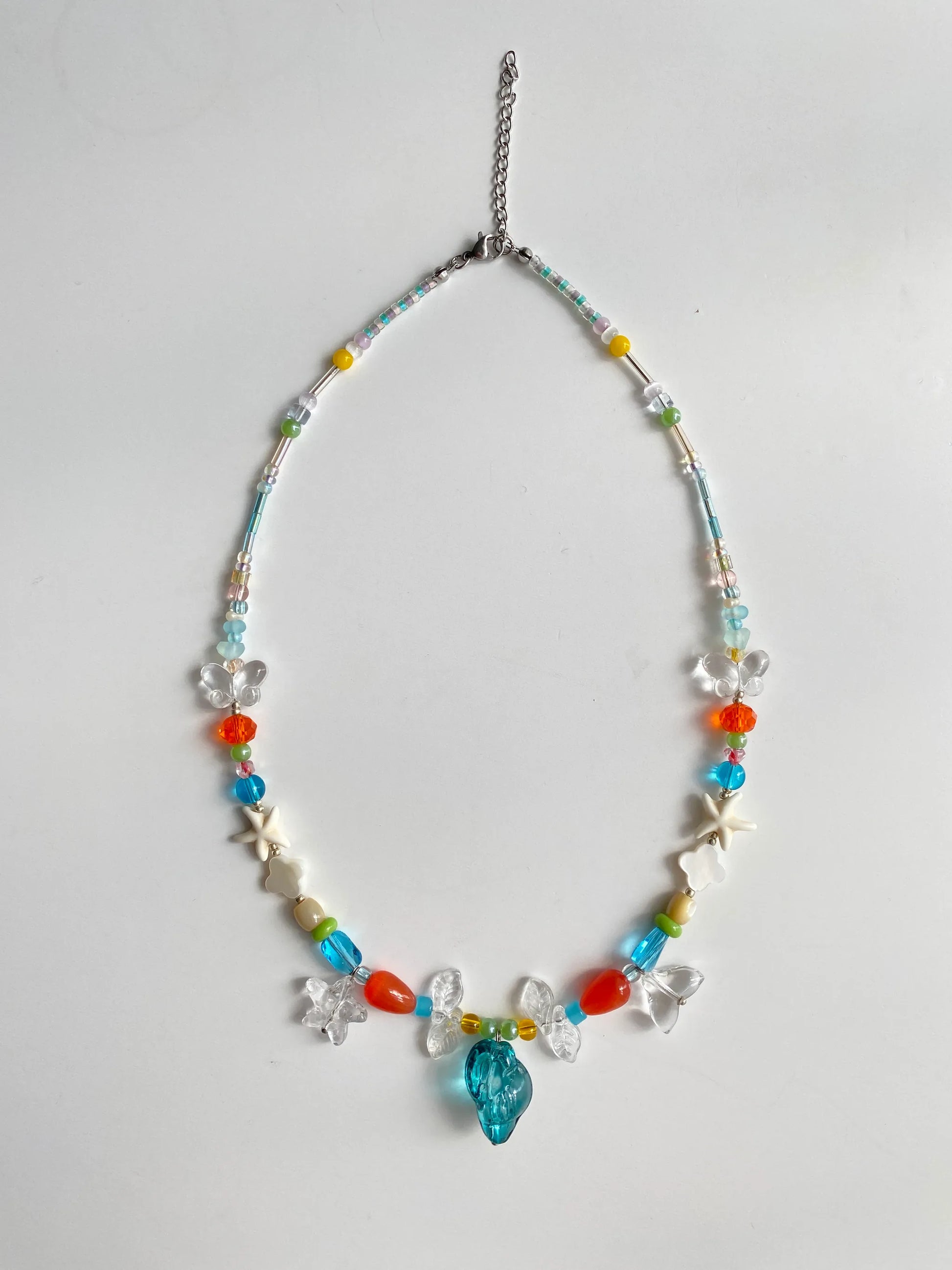Close-up of white glass fishtail and blue conch charms sparkling under the sun, showcasing artisanal textures.