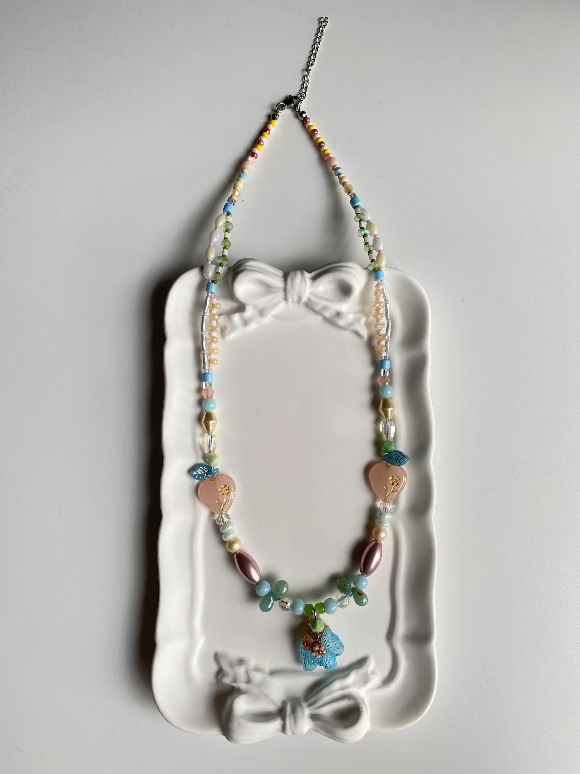 Close-up of an artisan beaded necklace with a floral dog charm and teardrop beads in a dish.