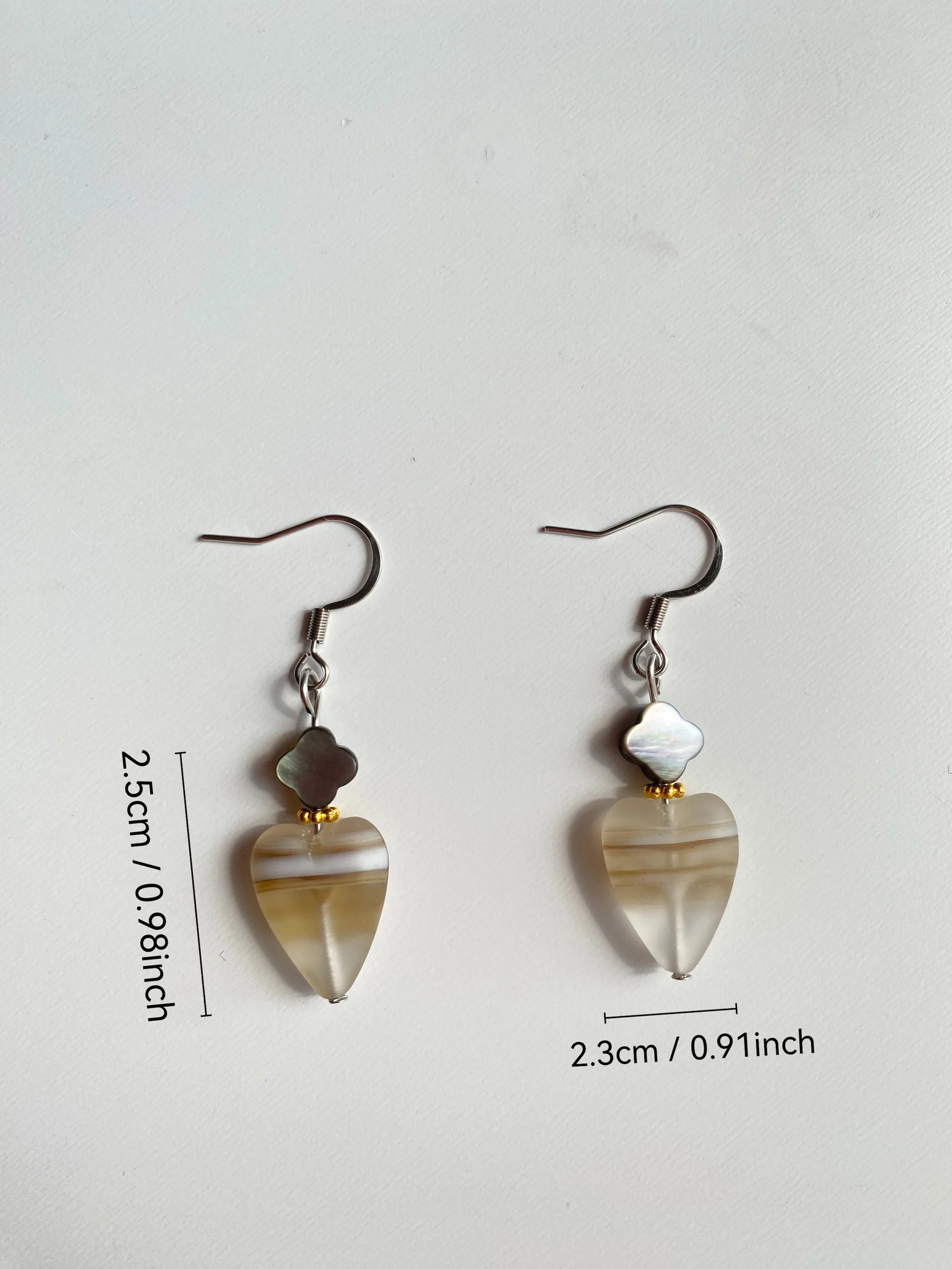 SKU Gilded Spacer: Frosted heart and black shell clover earrings with gold spacers, size in inches marked on a white desk.
