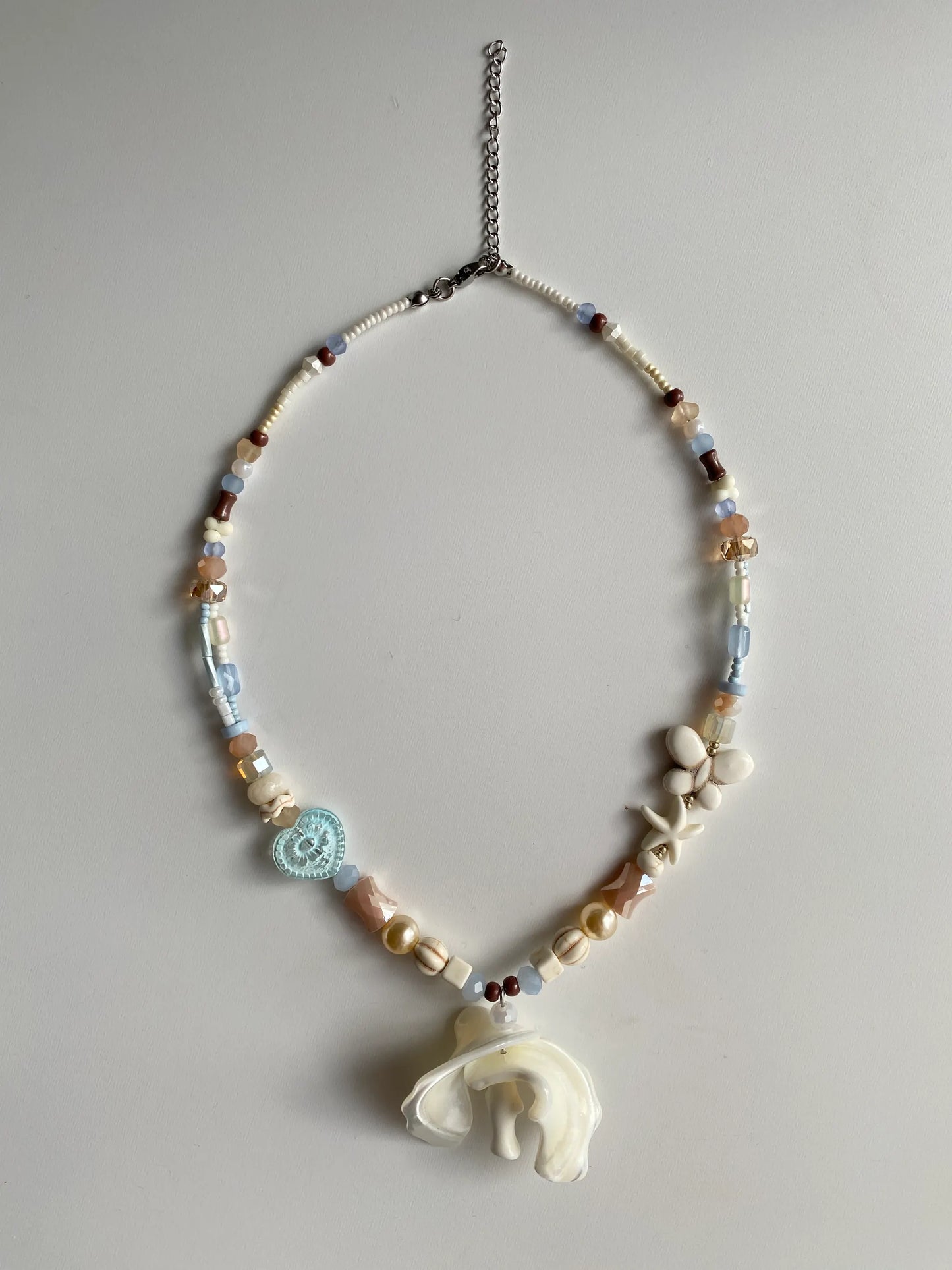 Detailed view of a unique handcrafted heavy workmanship necklace featuring white pine starfish, a fish, and iridescent shell pieces on a sunlit white desk.