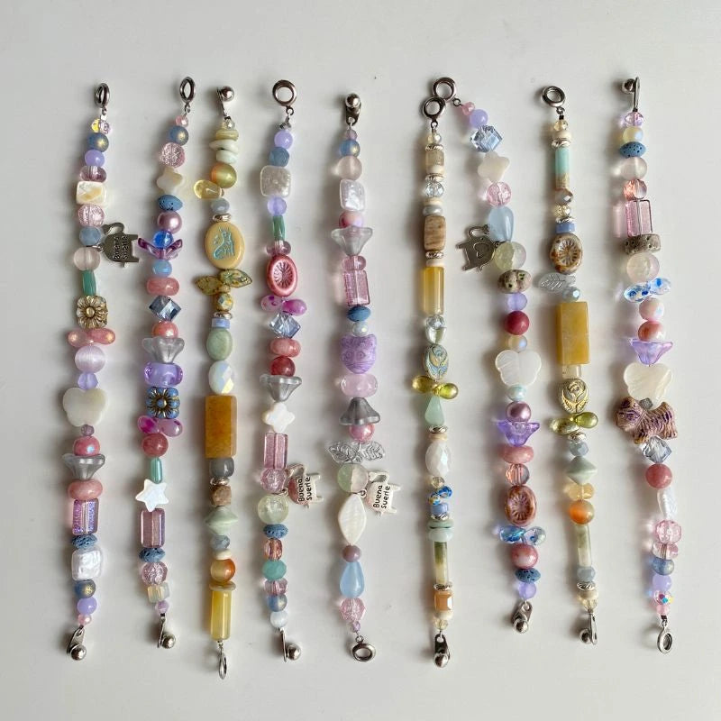 A whimsical collection of HuibenCraft handmade beaded bracelets in pastel pink, purple, and blue, featuring Czech glass, natural stones, and charms in butterfly, rose, and leaf shapes.