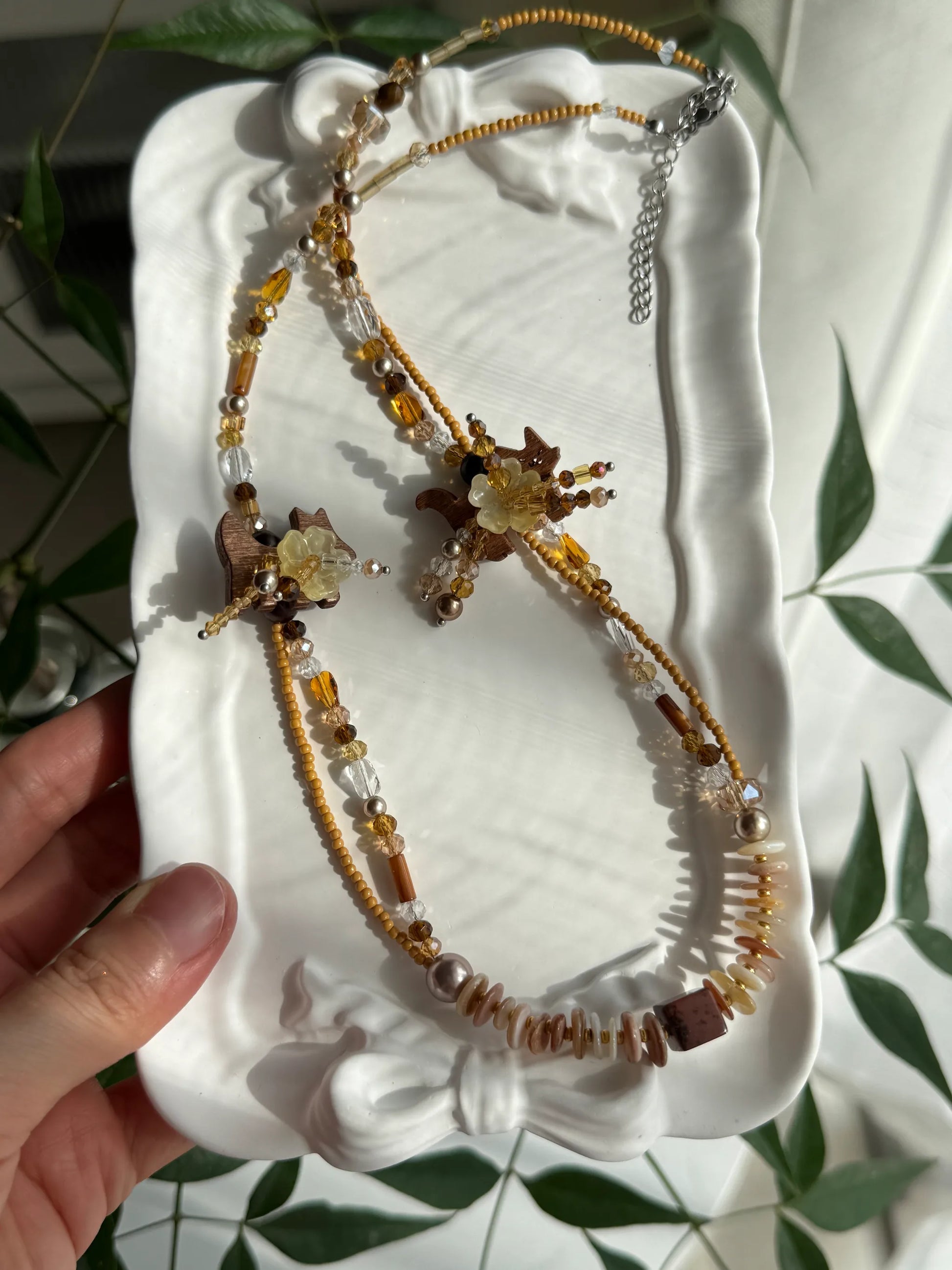 HuibenCraft 1-of-1 creative beaded necklace for pet lovers, featuring coconut shell animals and floral beadwork in a white ceramic dish.