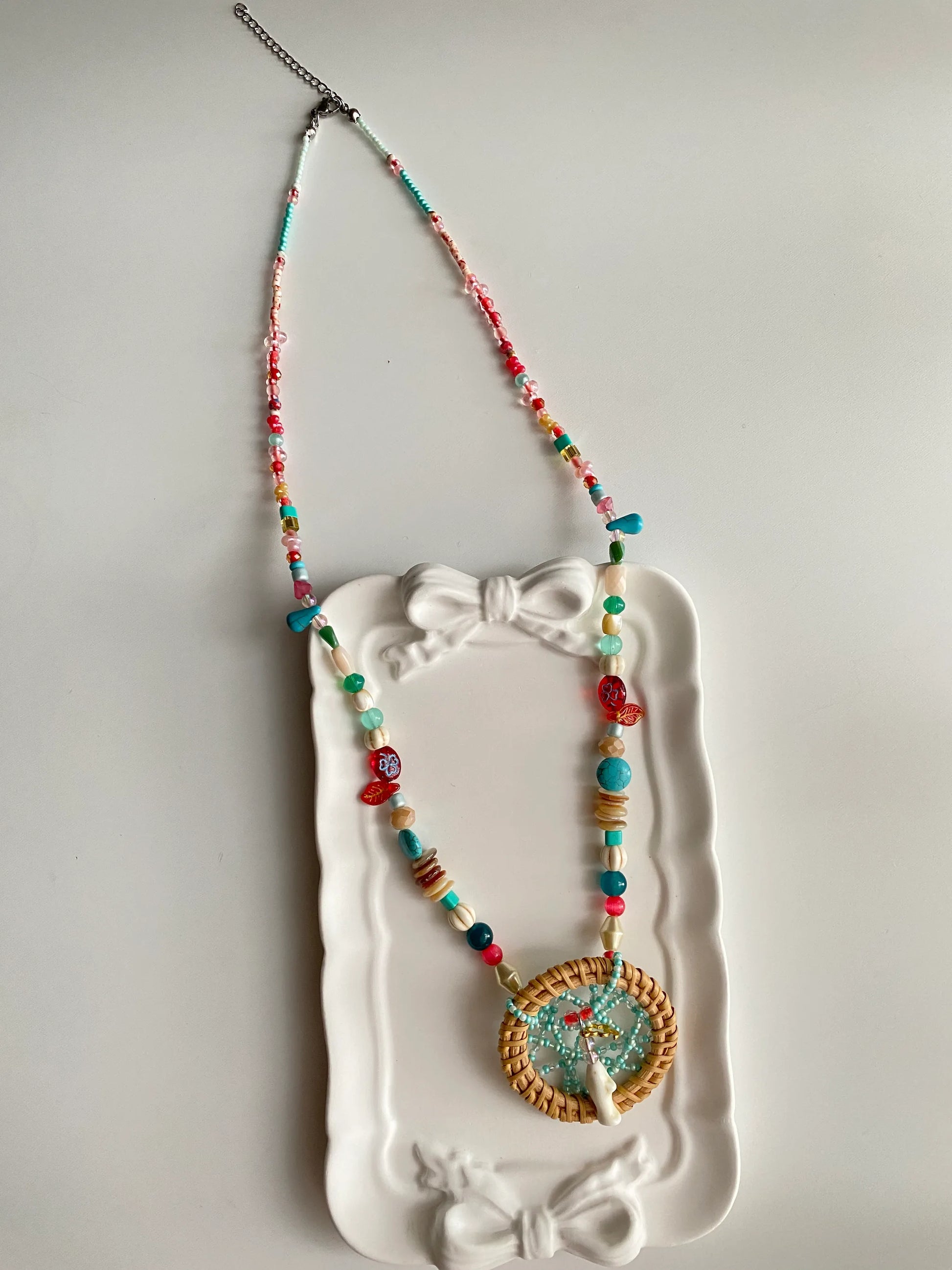 HuibenCraft 1-of-1 heavy-workmanship dreamcatcher necklace with white pine stone accents in a white ceramic dish, a unique artisan gift.