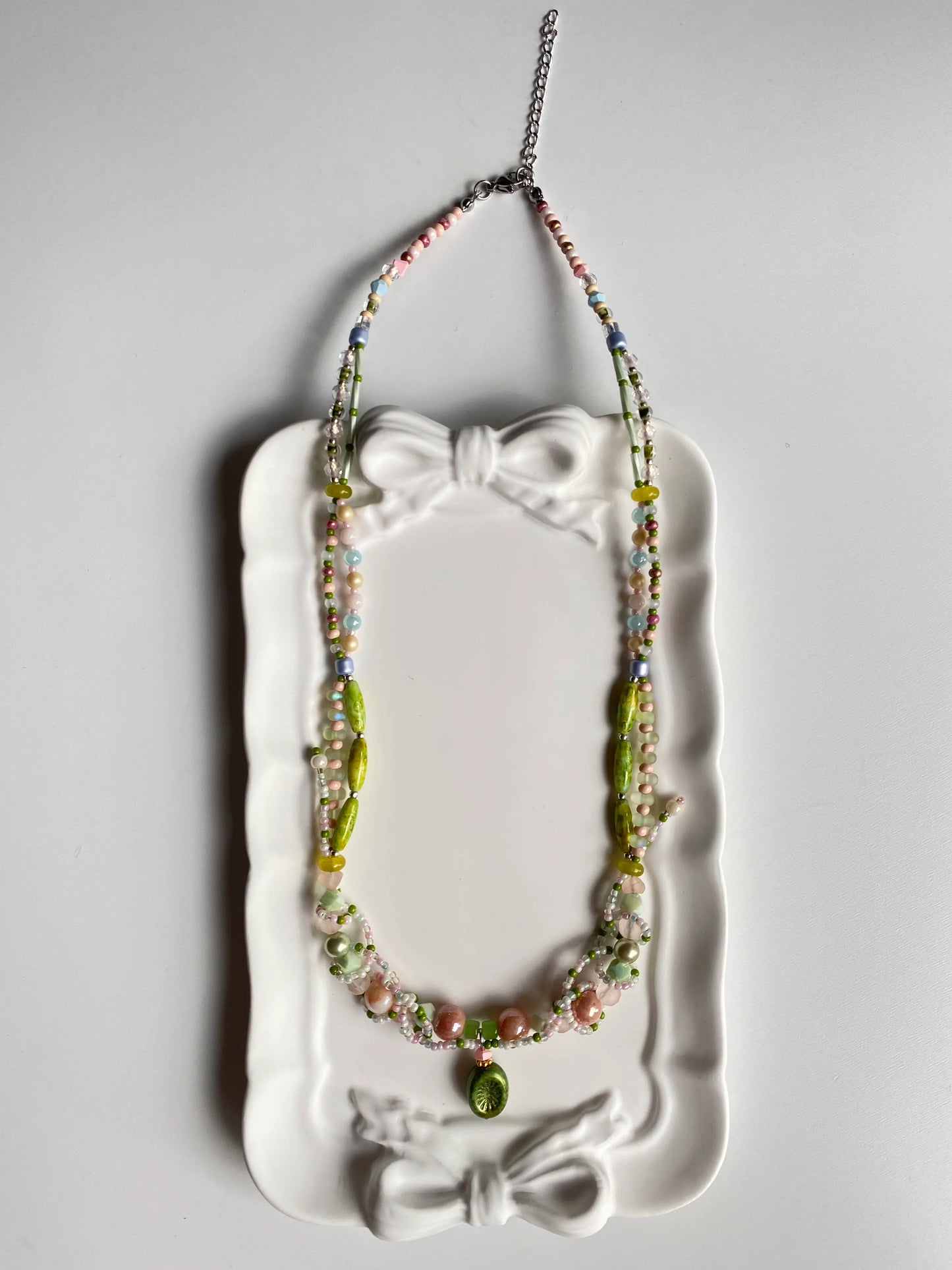 Close-up detail of a Czech glass kiwi pendant and intricate vine beadwork in a dish.