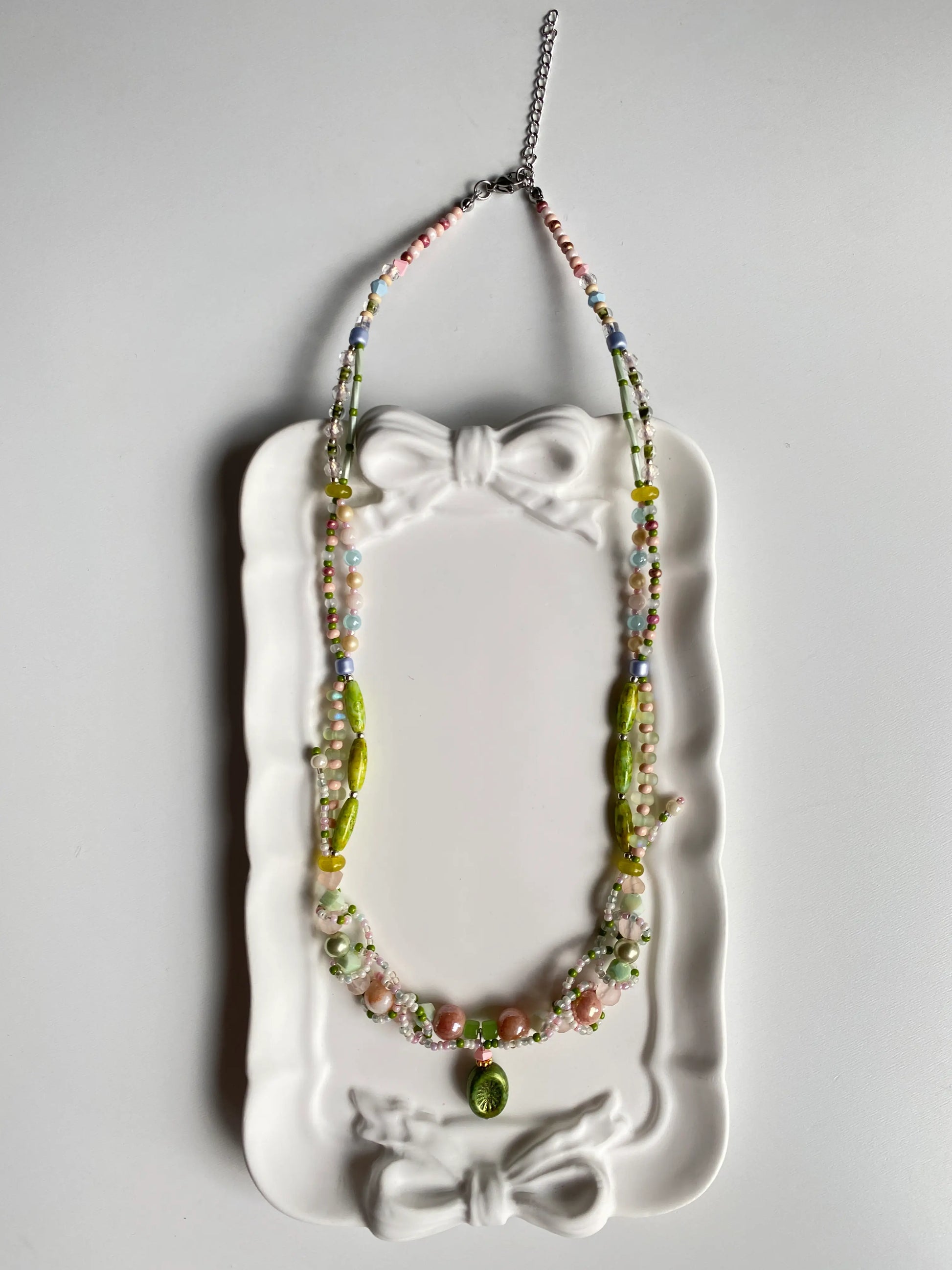 Close-up detail of a Czech glass kiwi pendant and intricate vine beadwork in a dish.