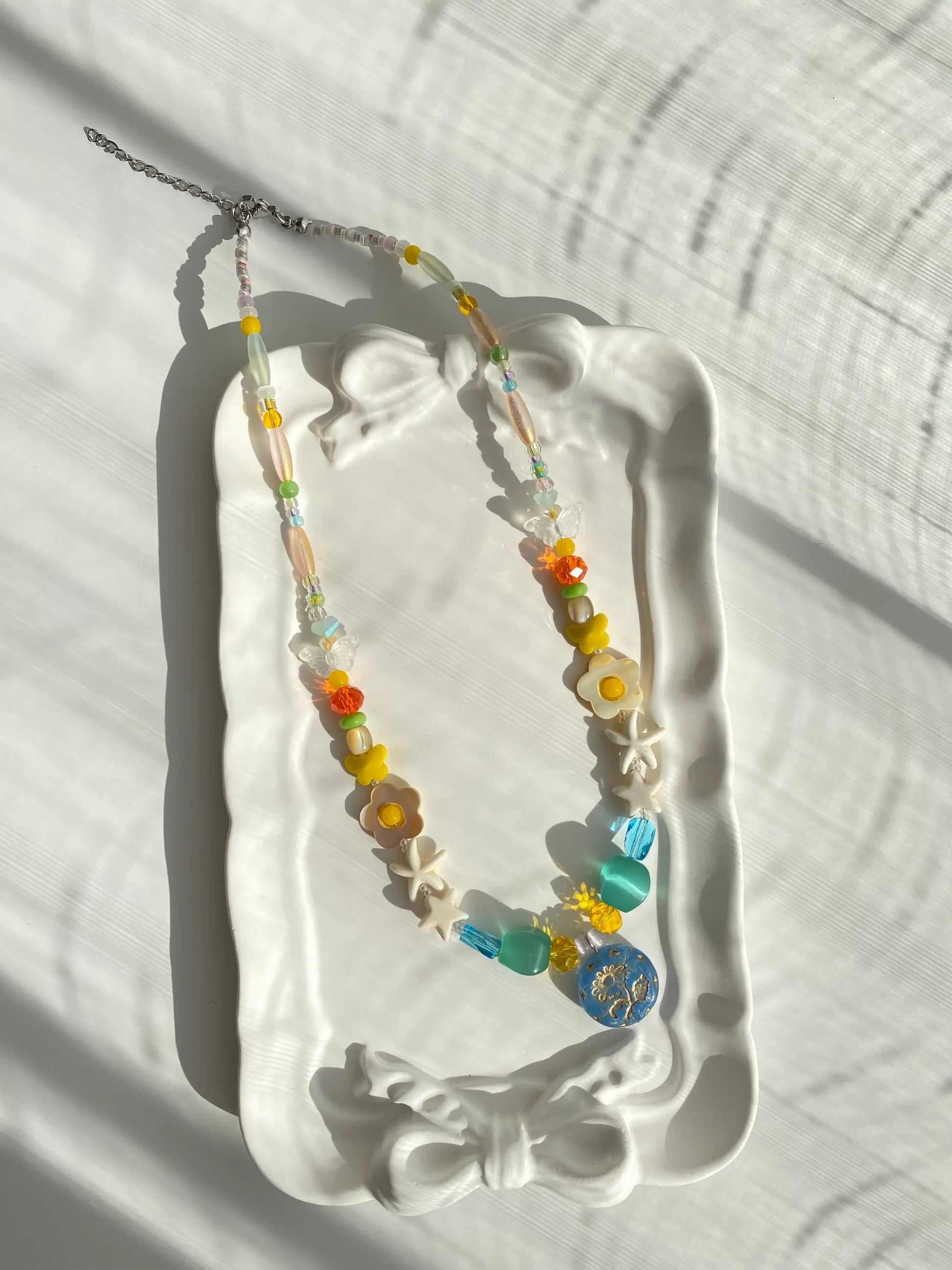 Detailed view of the Margaret flower beaded necklace resting in a white ceramic dish, highlighting its ocean-inspired palette.