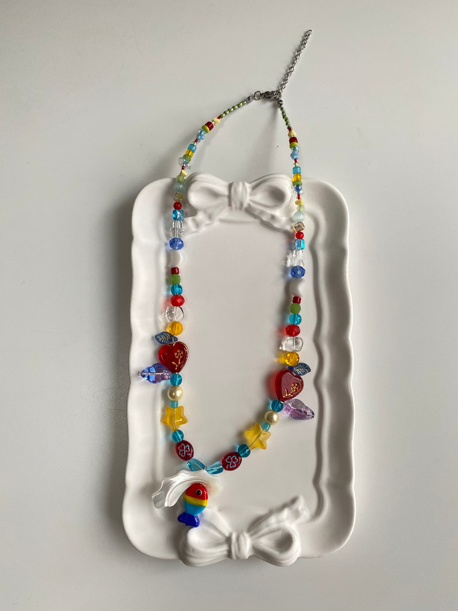 Rainbow Czech glass fish necklace displayed flat, featuring a natural Triton shell pendant, moon shell charm, colorful beads and summer coastal details.