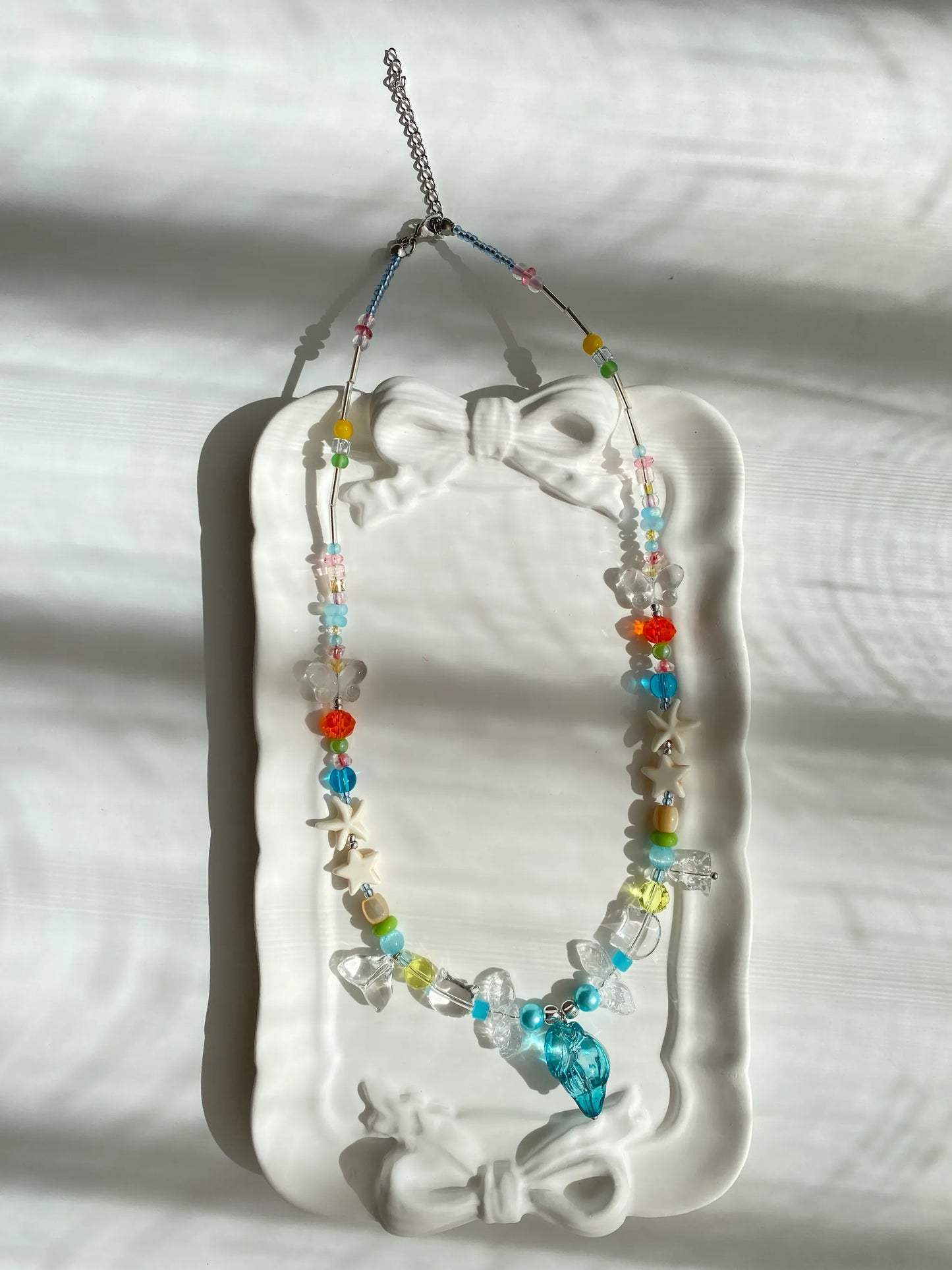 Handcrafted 1-of-1 necklace with a glass sea conch and quirky charms resting in a stylish jewelry dish.