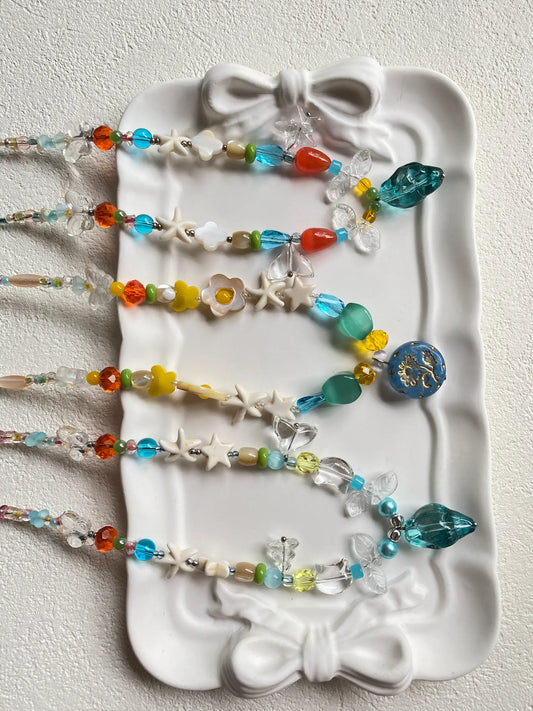Close-up of handcrafted jewelry details showing translucent glass beads, starfish charms, and white turquoise stars in the sun.