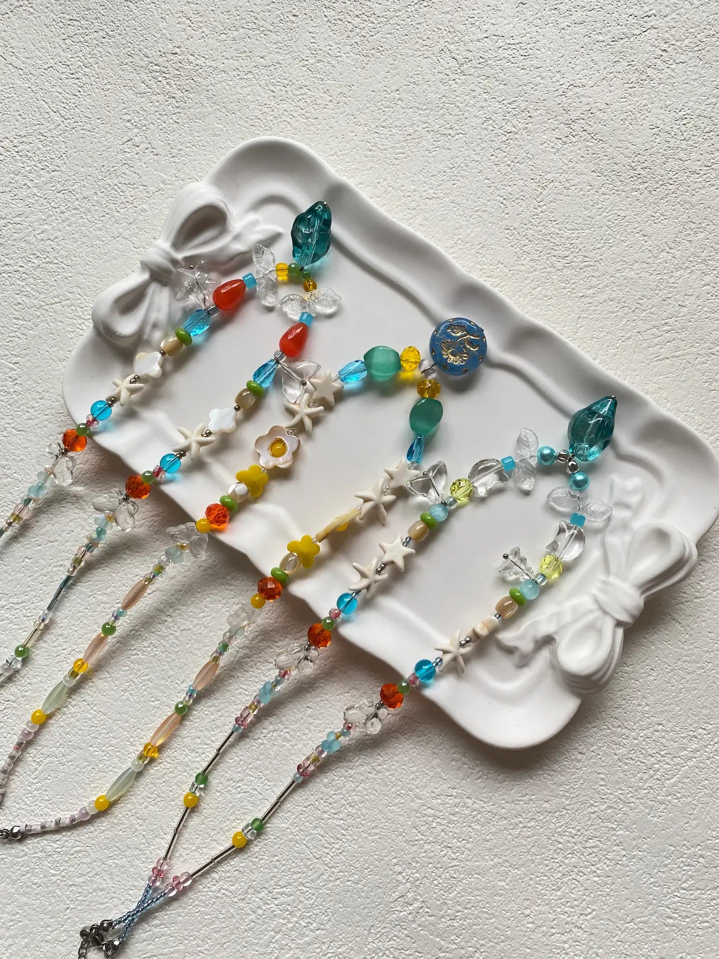 Top-down view of three unique summer beaded necklaces with eclectic shells, glass fish tails, and blue conch pendants.
