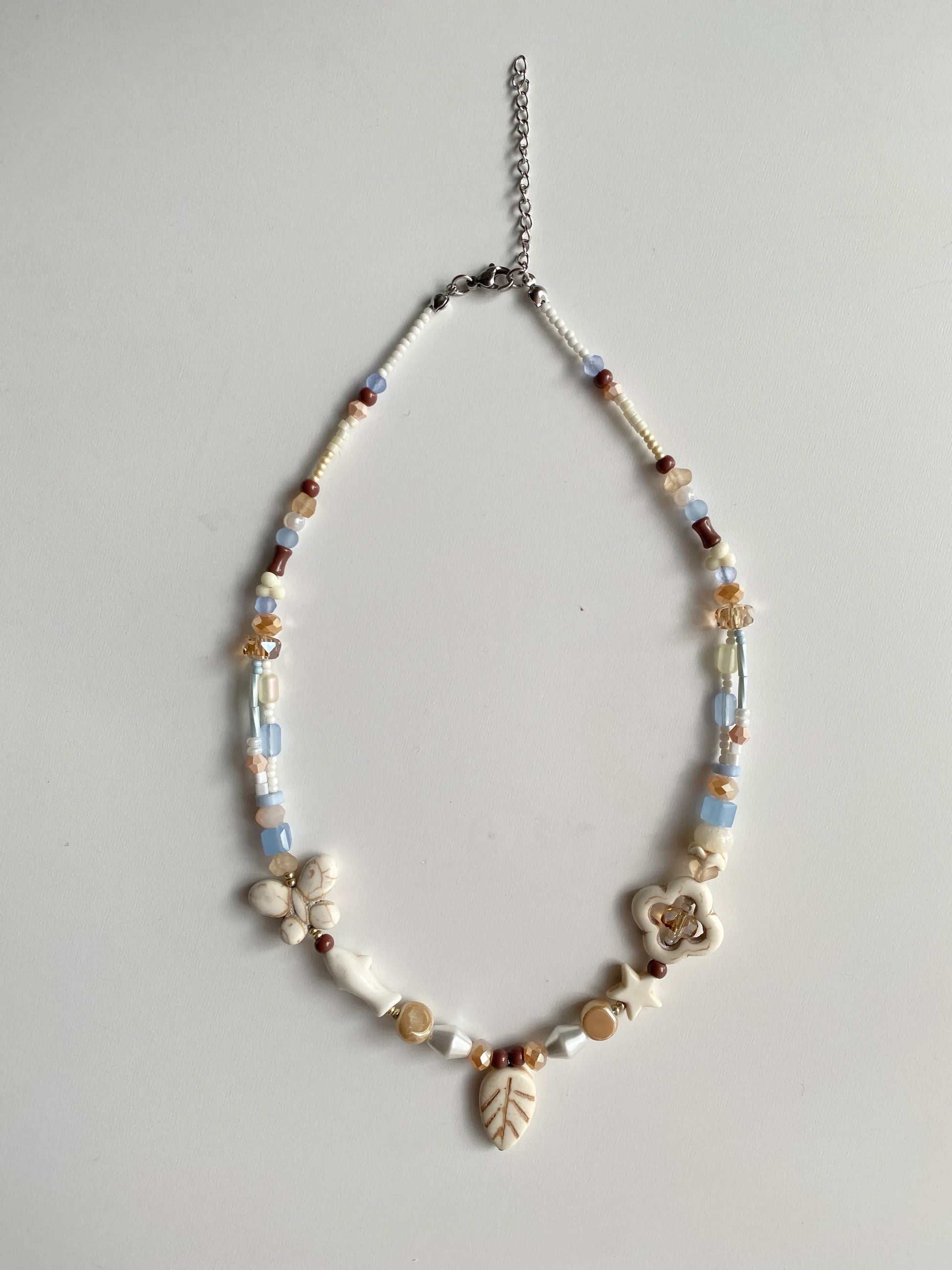 Detailed view of an ocean-themed necklace featuring hollow clovers, star and fish-shaped white pine stones, and sparkling beads on a sunlit white desk.