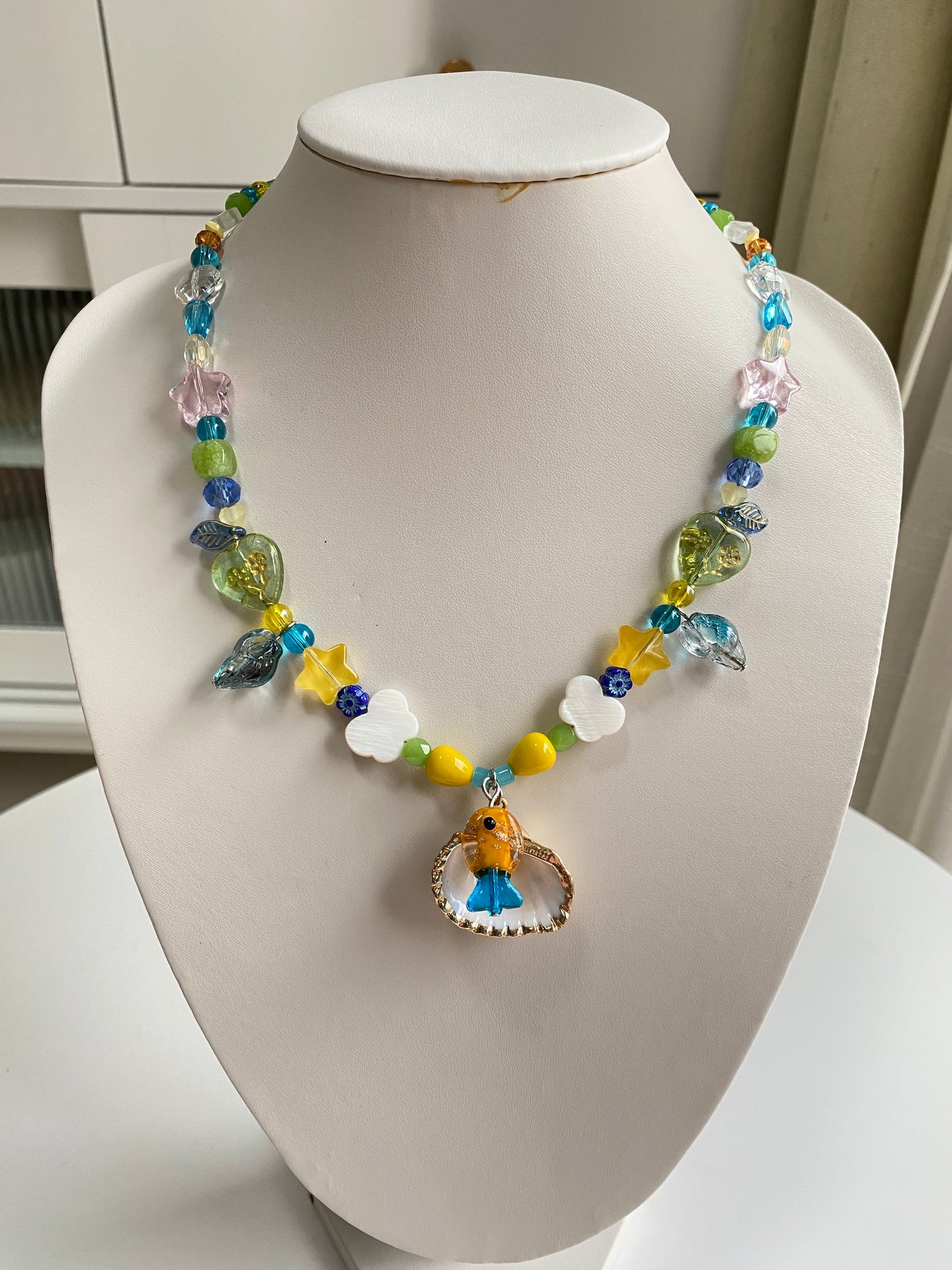 One-of-one shell necklace displayed on a necklace bust with colorful Czech glass fish, butterfly shell accents and handcrafted summer beadwork.