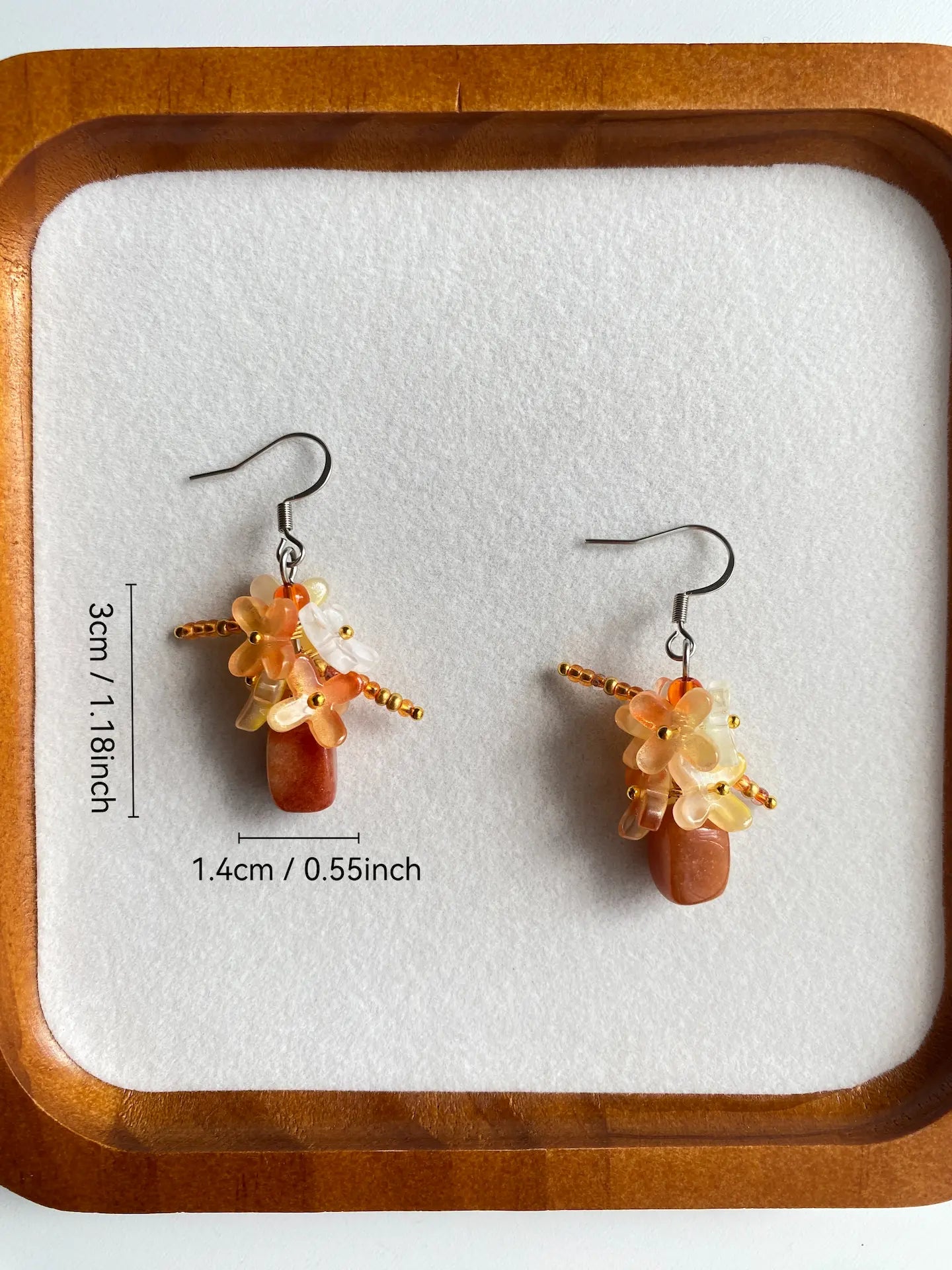 Size measurement in inches of the majestic orange stone and golden floral beaded earrings with stainless steel hooks, displayed in a white dish.