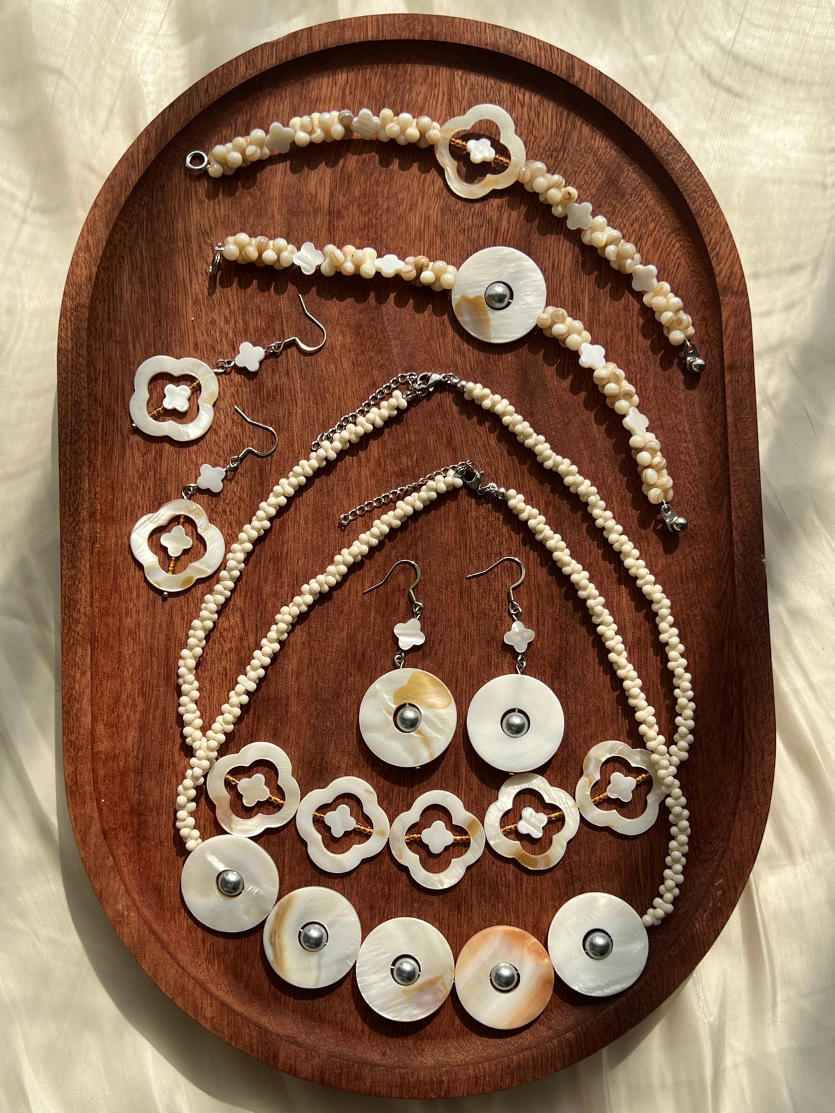 HuibenCraft Pacific Shell Collection featuring two handmade shell jewelry sets with necklaces, bracelets, and earrings arranged on a wooden plate.