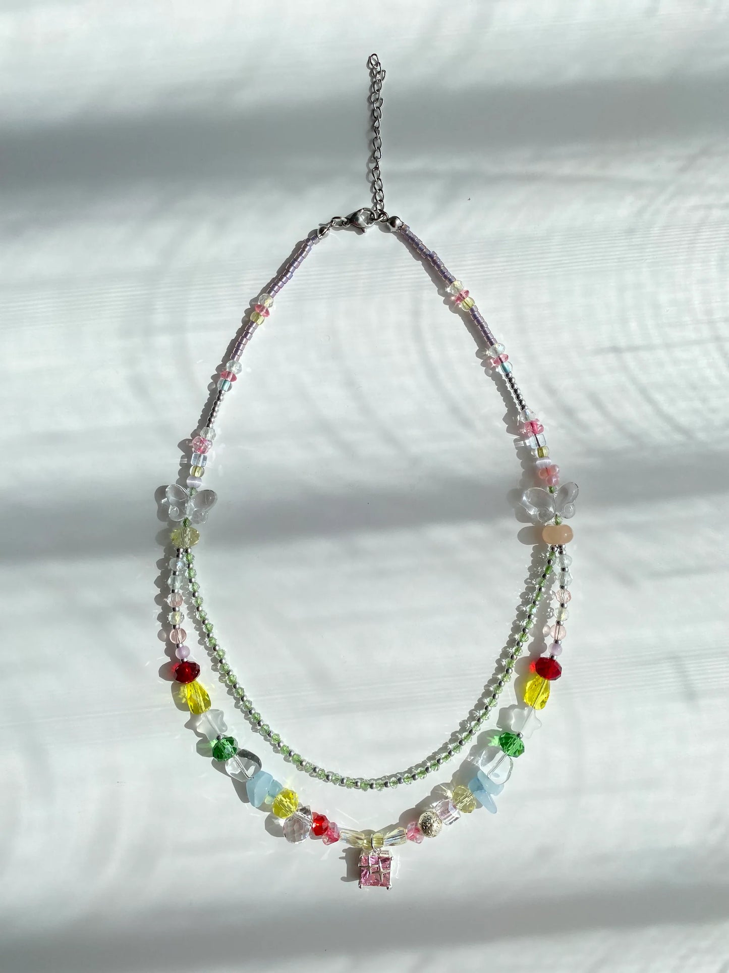 Minimalist and fashionable colorful seed bead necklace with a pink glass pendant and frosted star accents, flat lay on a table.