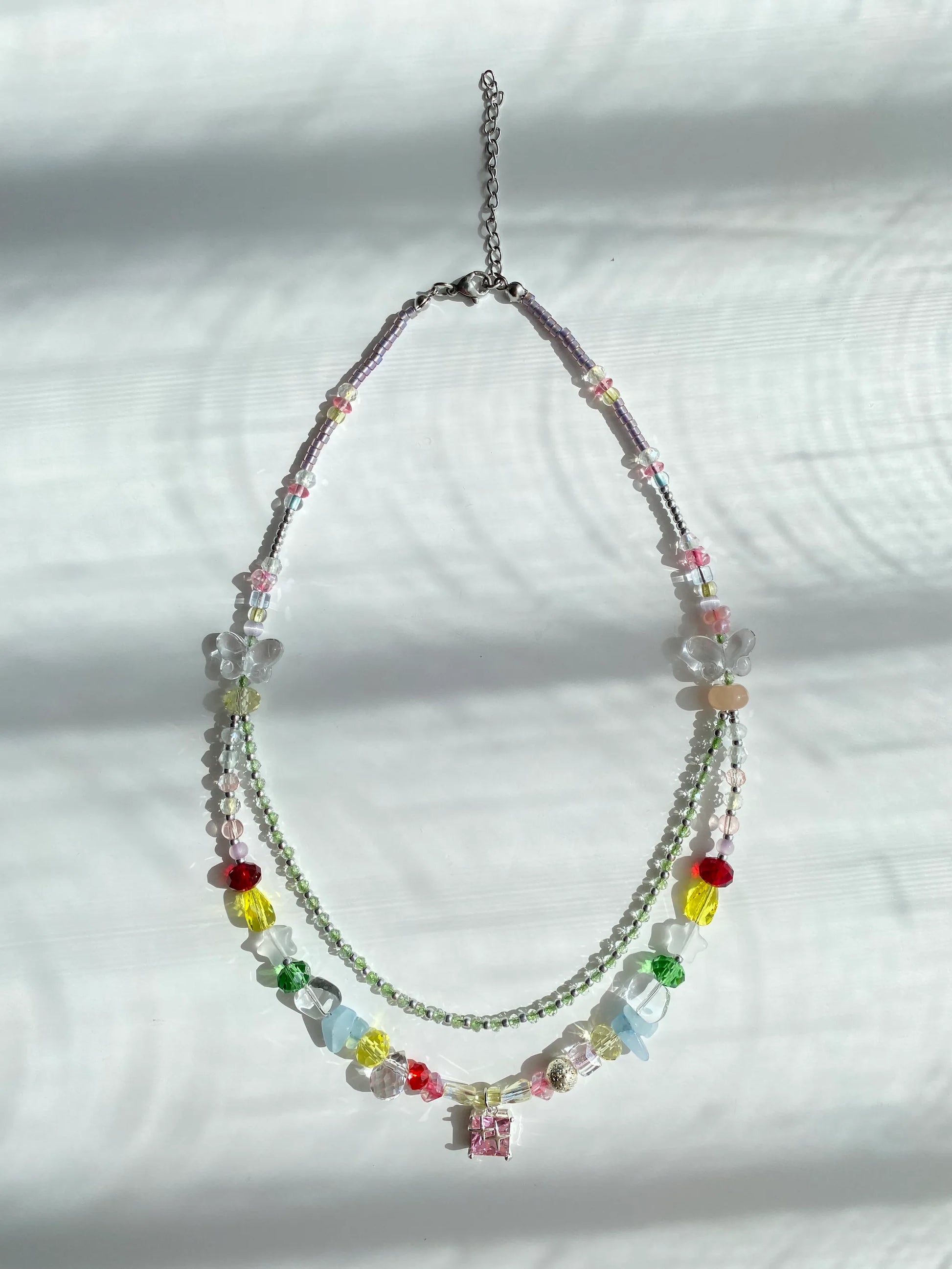 Minimalist and fashionable colorful seed bead necklace with a pink glass pendant and frosted star accents, flat lay on a table.