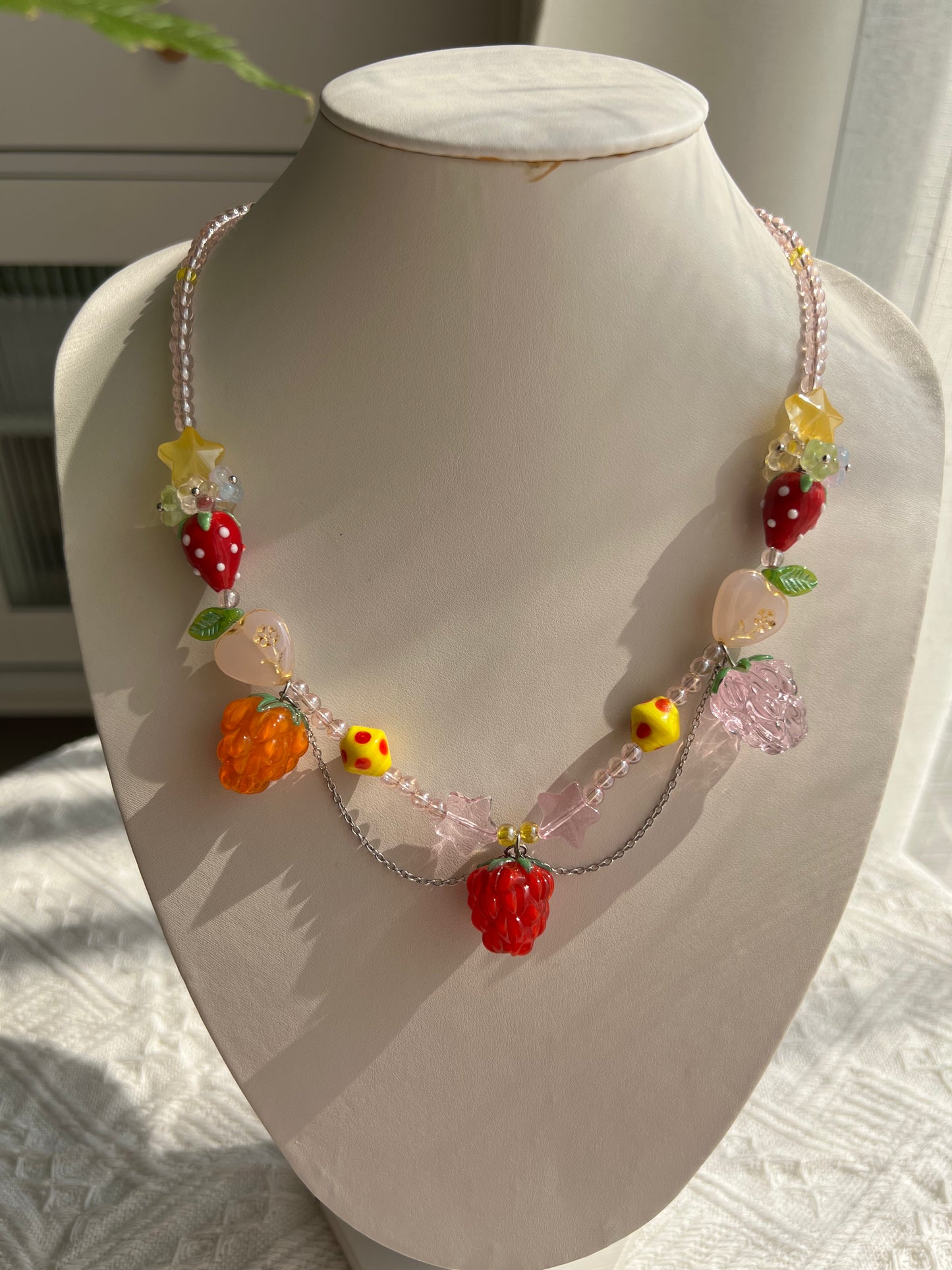 Playful Raspberry Necklace displayed on a necklace bust, showing its fruit beads and pendant.