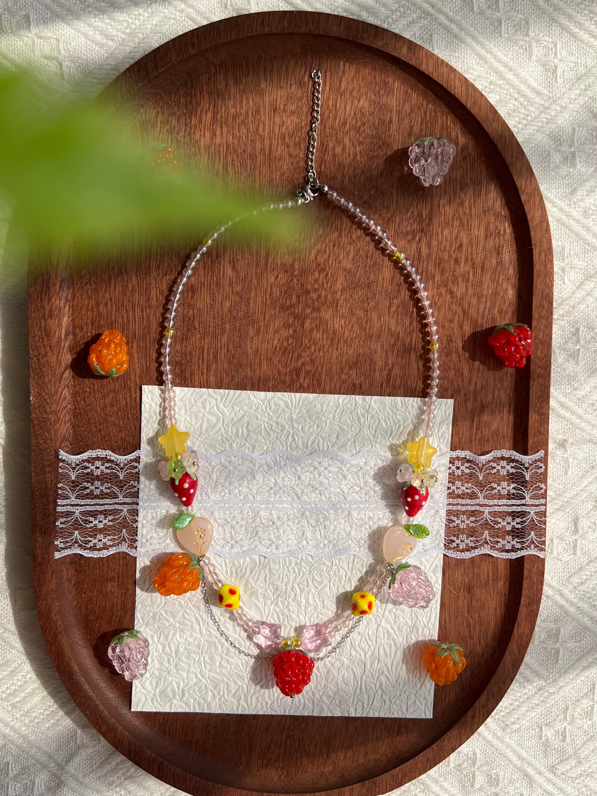 Playful Raspberry Necklace arranged on a wooden tray with raspberry beads nearby.