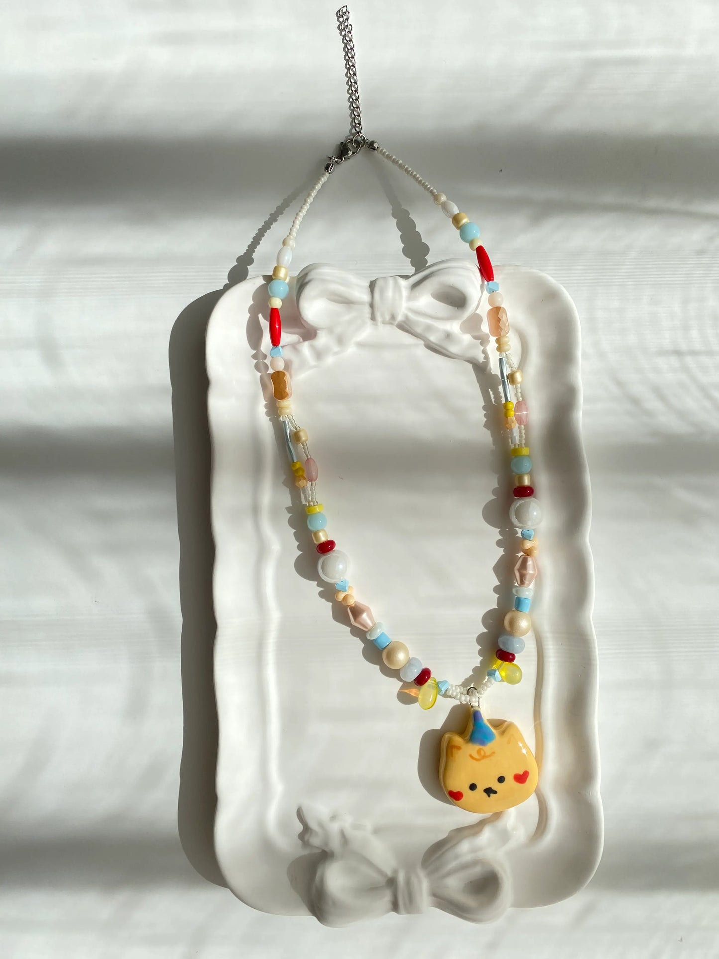 Close-up of a unique handmade necklace featuring a ceramic bear and pearl beads in a dish.