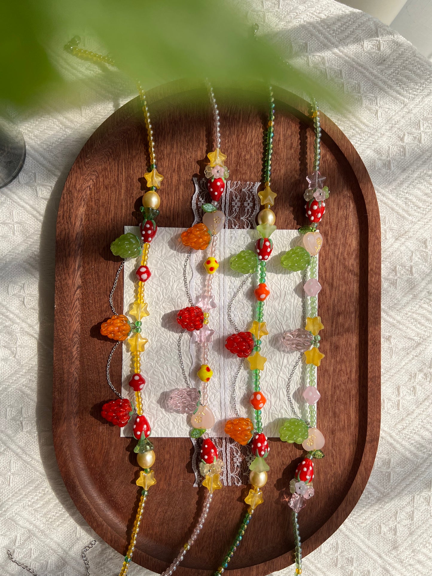 Four colorful fruit bead necklaces displayed together on a wooden tray.