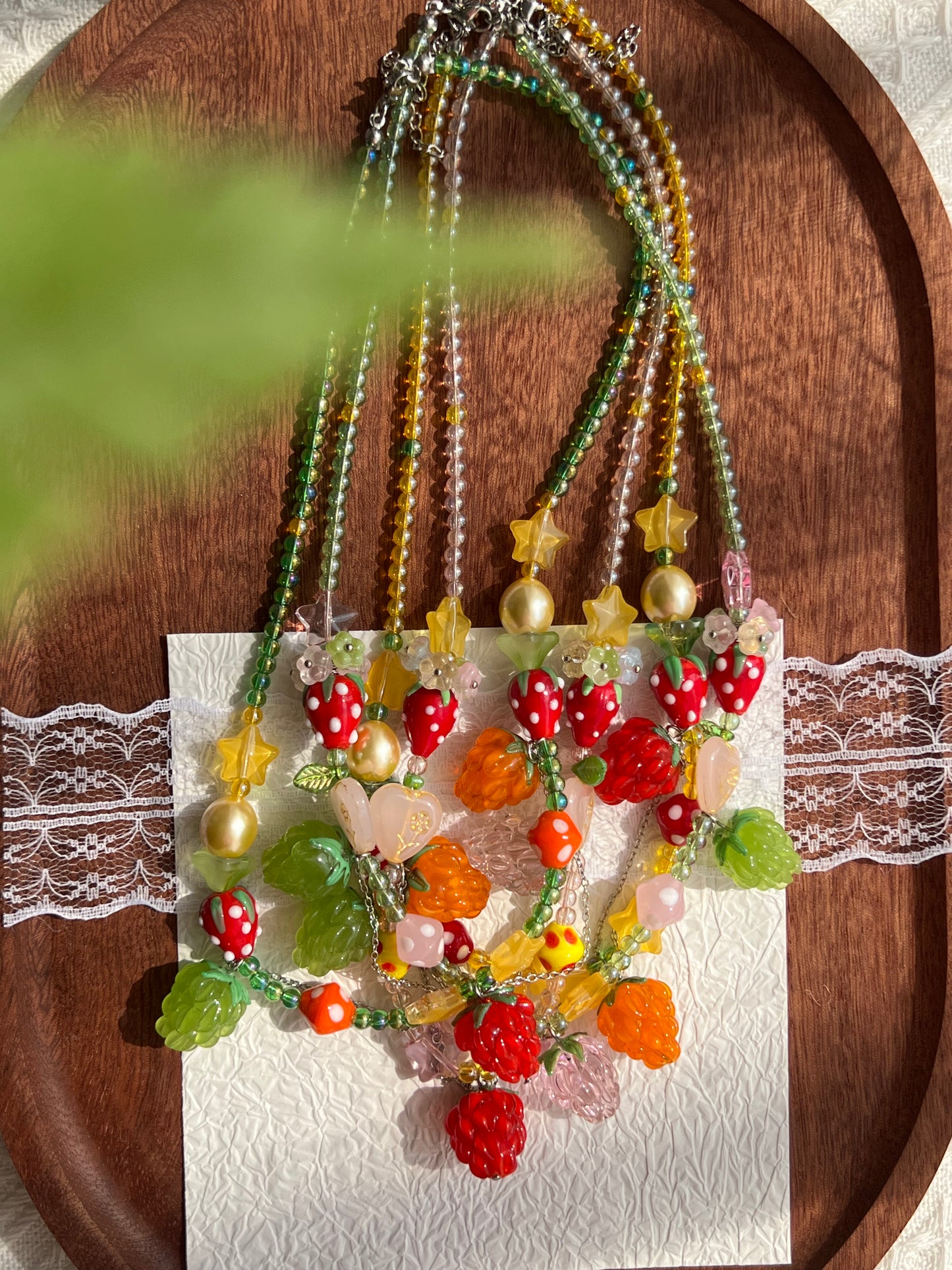 Full overhead view of four colorful raspberry and strawberry necklaces arranged together on a wooden tray.