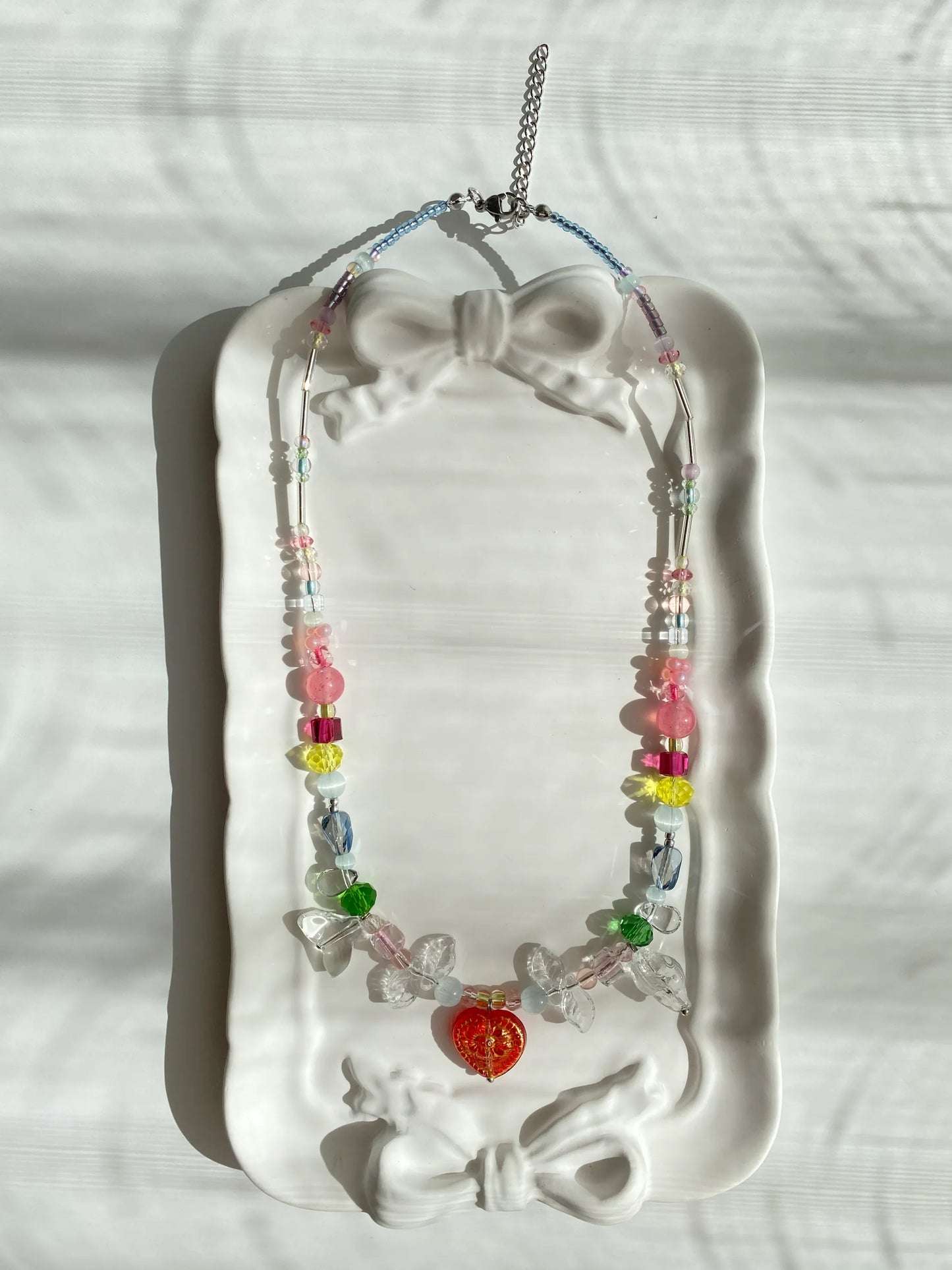 Unique HuibenCraft beach-ready colorful necklace with a red heart pendant and glass leaf accents, sparkling beautifully inside a dish under natural light.