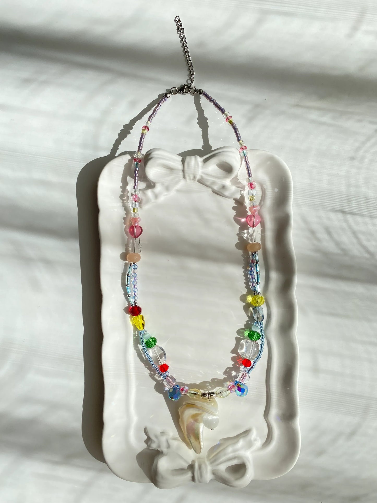 Unique HuibenCraft seed bead layered necklace featuring pink hearts and bear beads with a shell pendant, displayed in a decorative dish.
