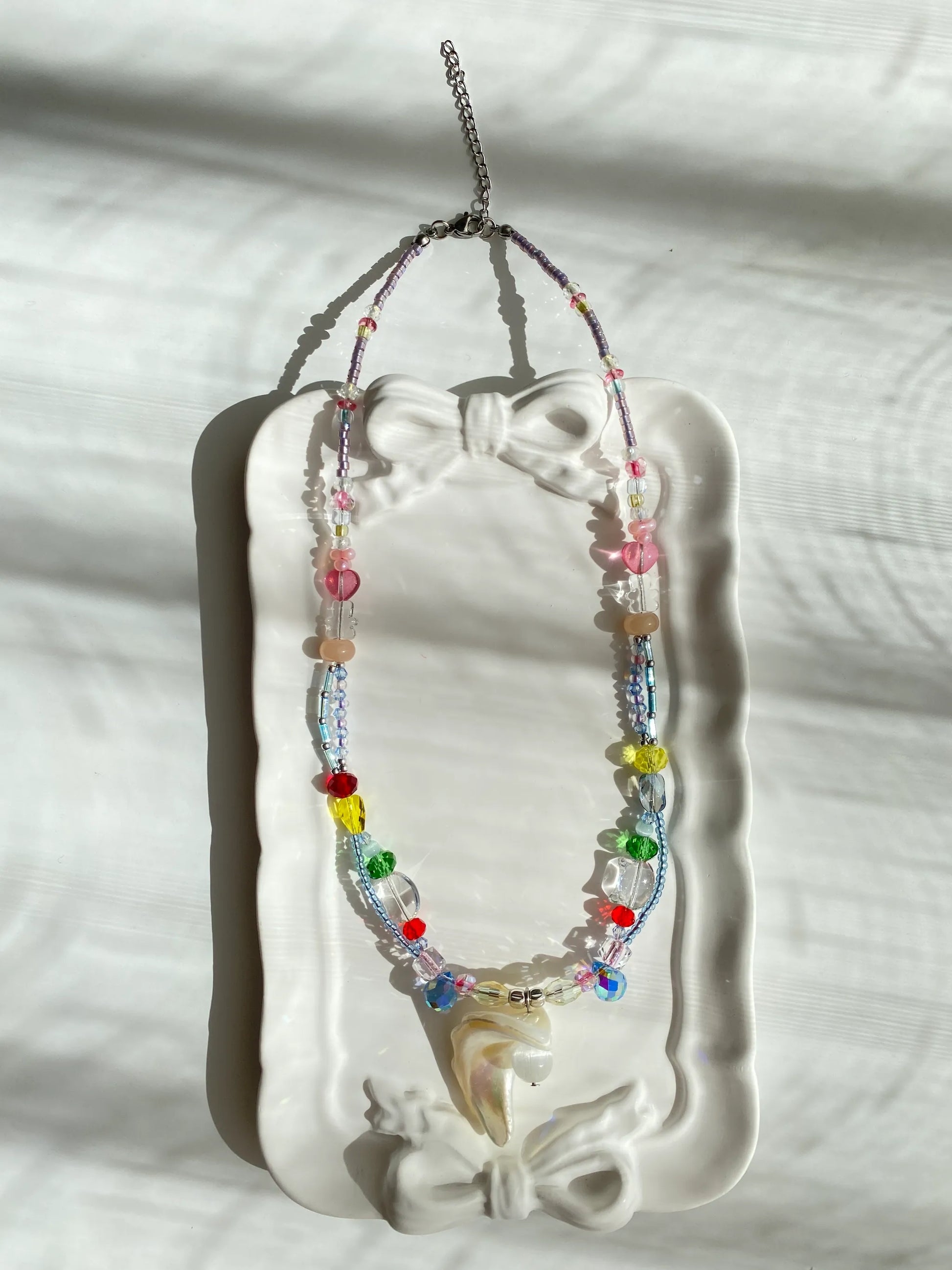 Unique HuibenCraft seed bead layered necklace featuring pink hearts and bear beads with a shell pendant, displayed in a decorative dish.