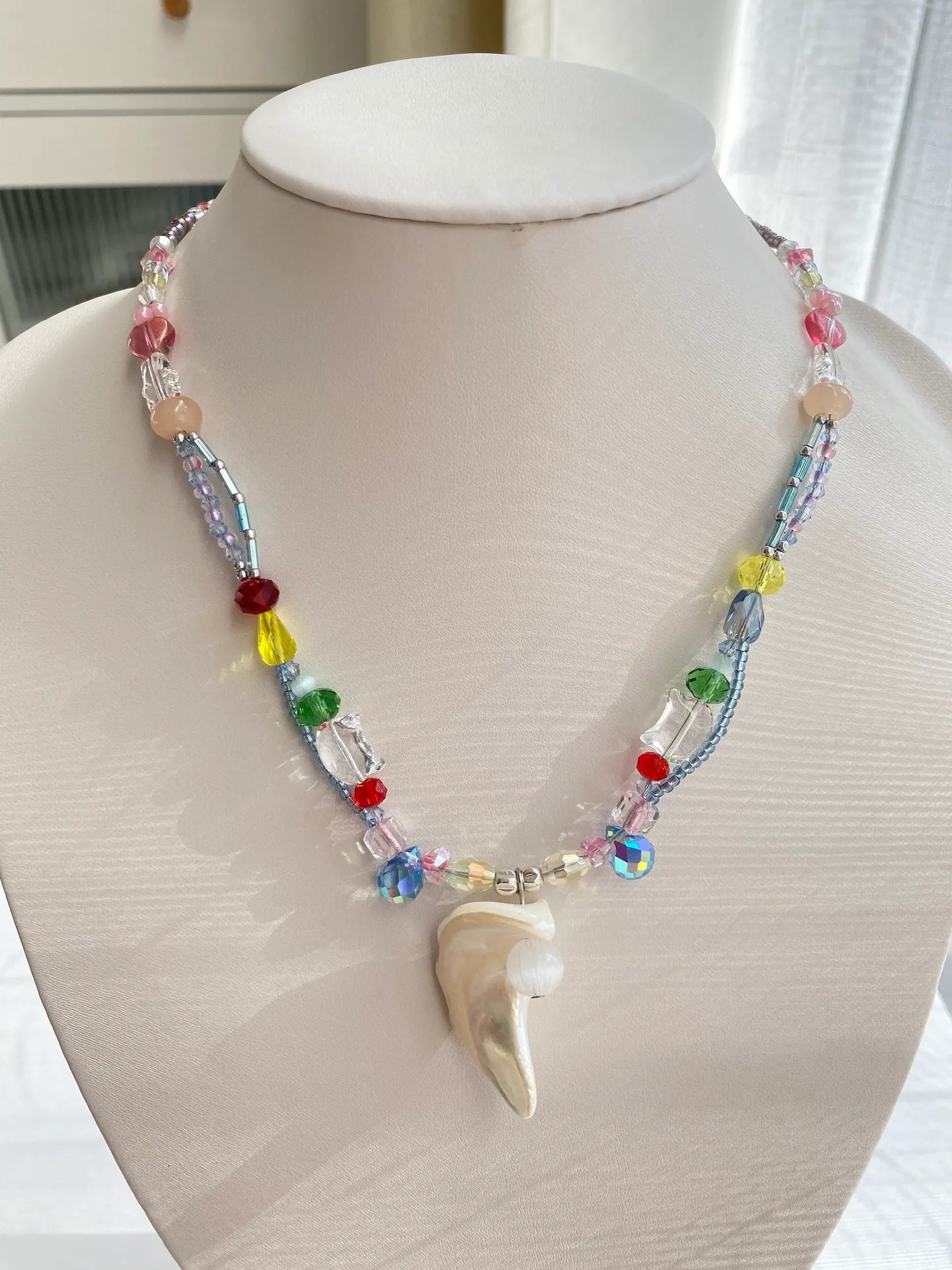 HuibenCraft 1-of-1 colorful seed bead choker with a button shell pendant on a jewelry mannequin under bright, glittering natural sunlight.