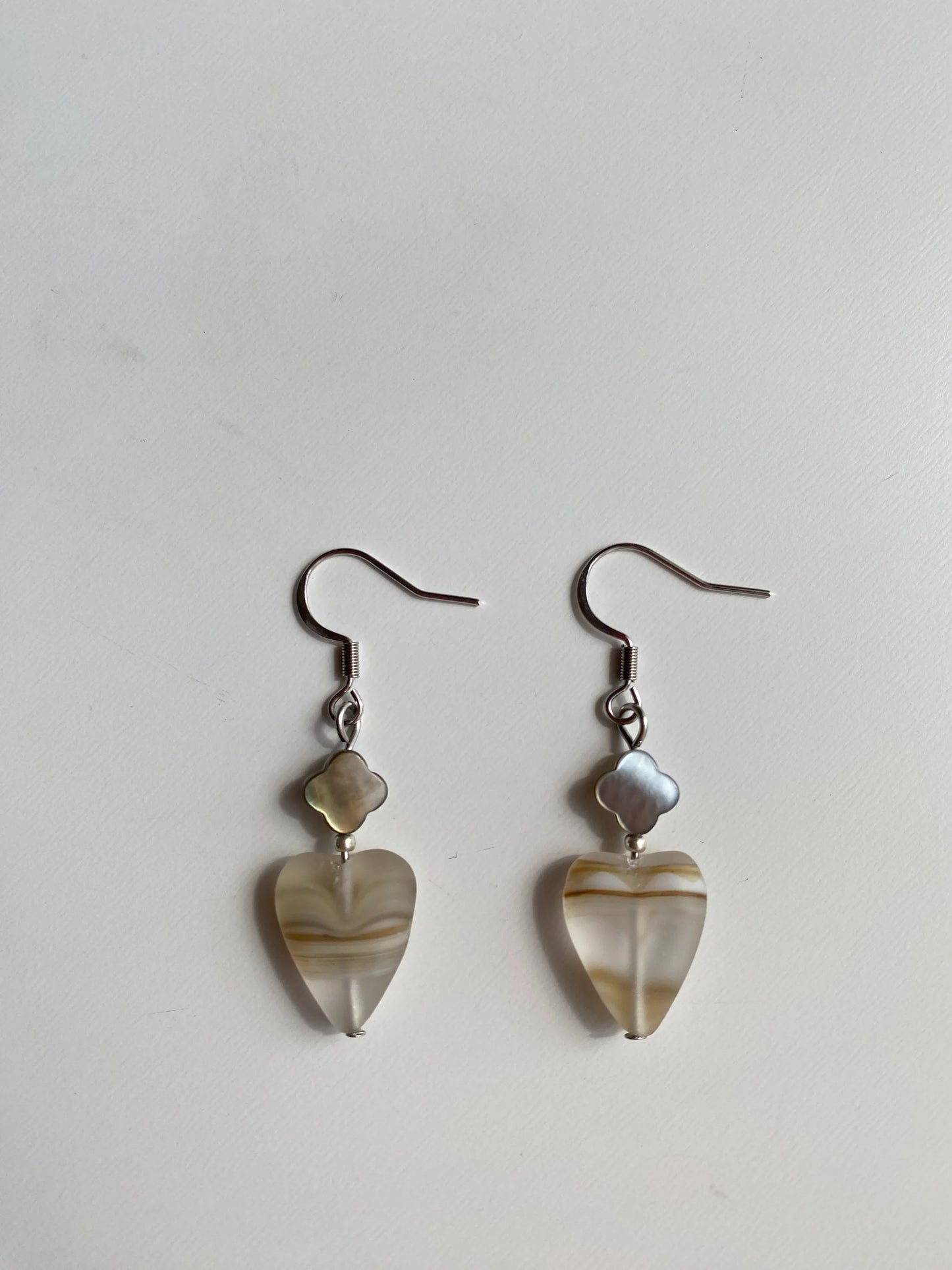 SKU Silver Sparkle: Minimalist retro frosted heart and black clover earrings with shimmering silver seed beads on a white desk.