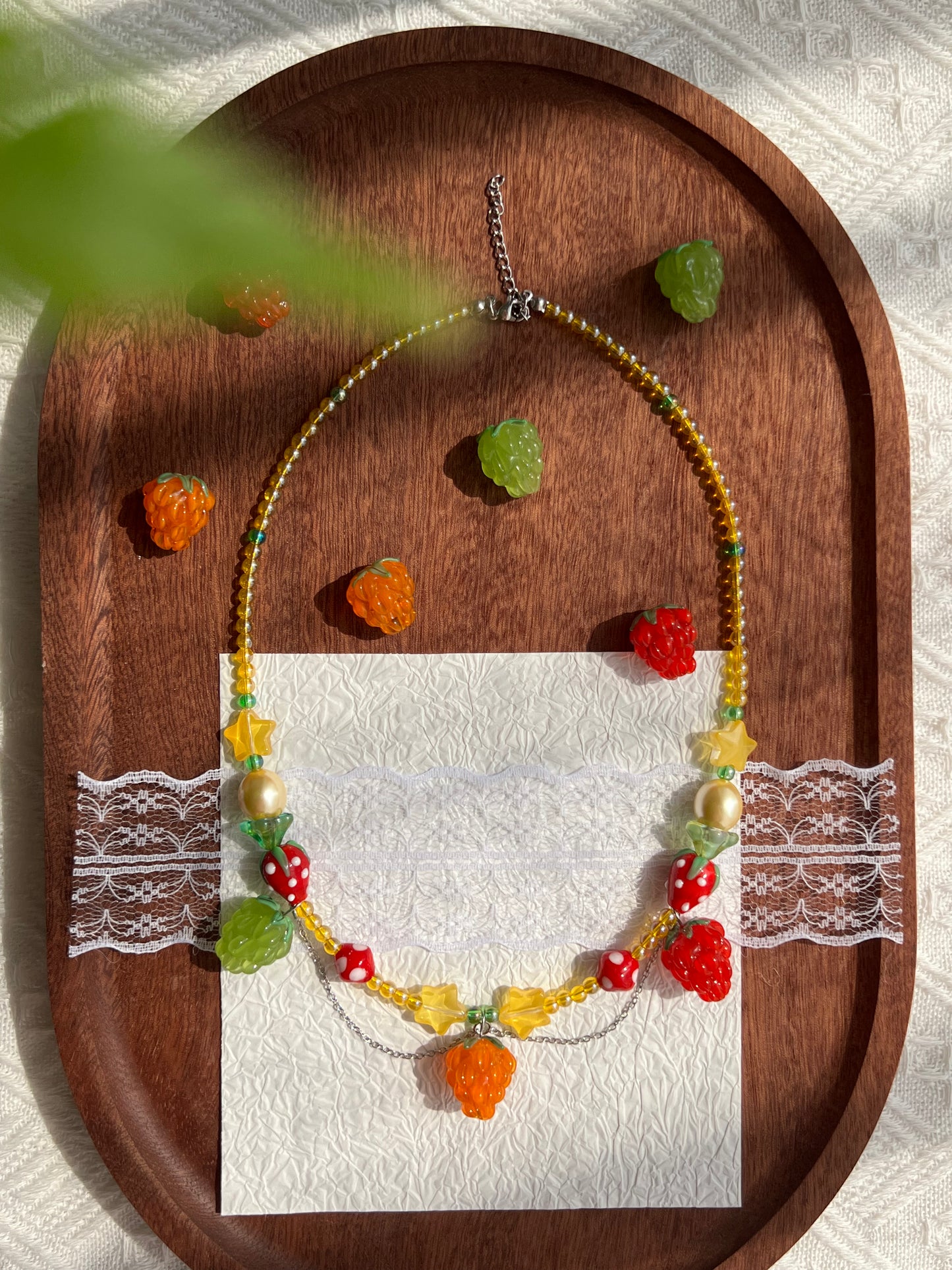 Sweet Raspberry Strawberry Necklace arranged on a wooden tray with raspberry beads nearby.