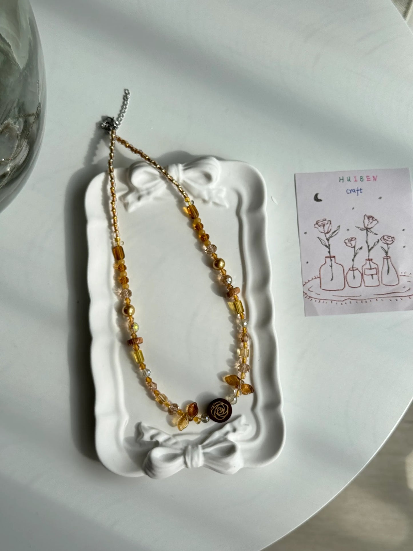 HuibenCraft 1-of-1 minimalist beaded necklace with a wooden floral rose pendant, elegant for office or date wear, placed in a white ceramic dish.