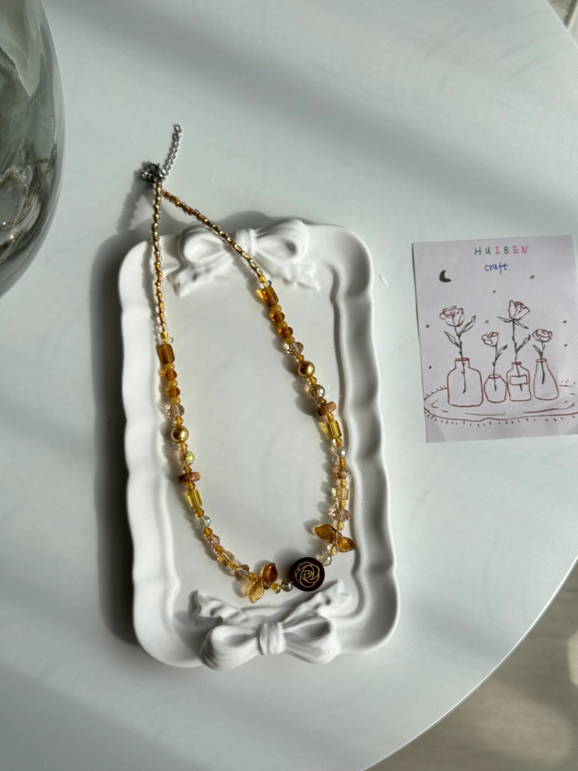 HuibenCraft 1-of-1 minimalist beaded necklace with a wooden floral rose pendant, elegant for office or date wear, placed in a white ceramic dish.